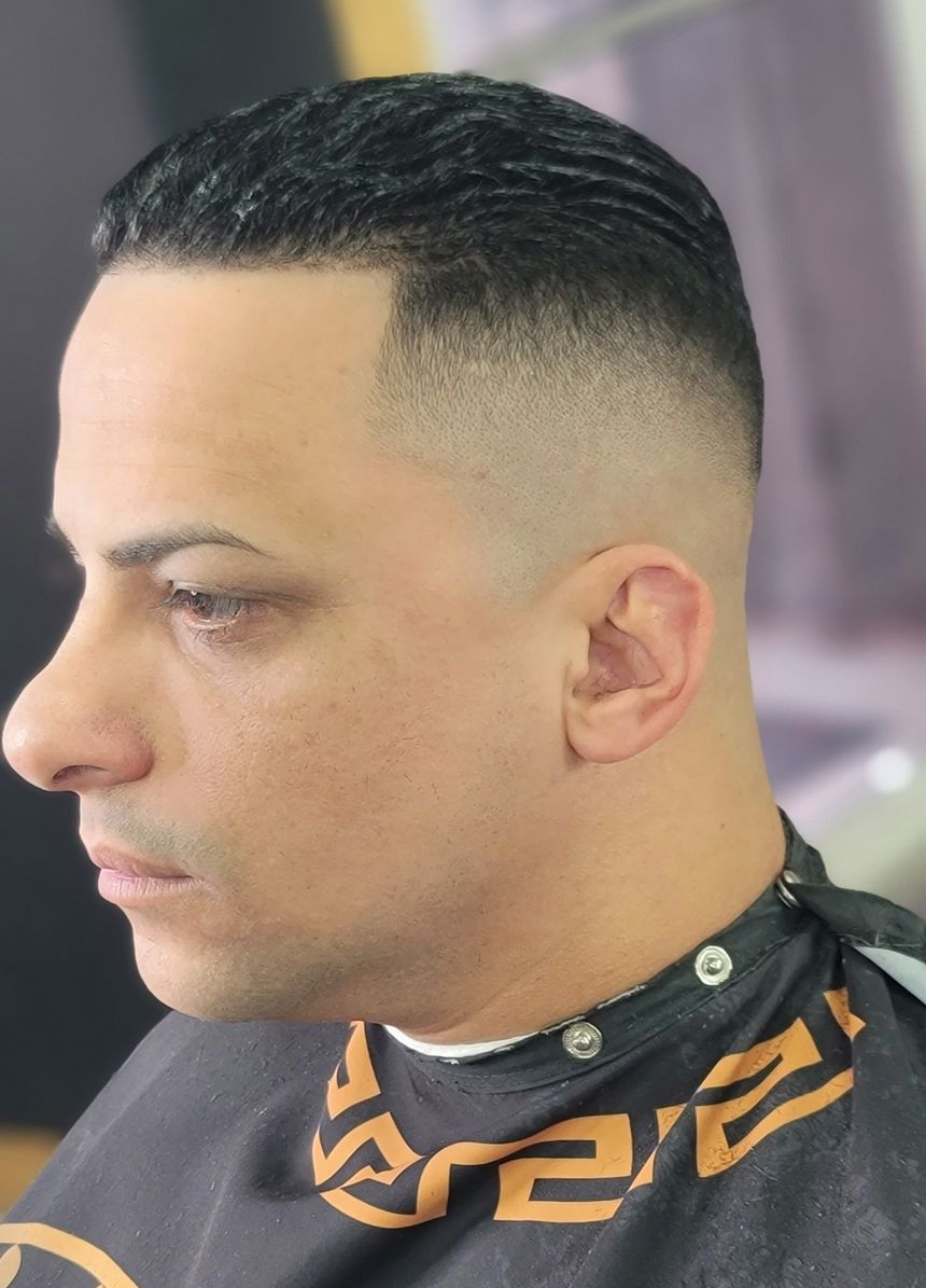 Man with brown skin, a patterned haircut, and a gold earring. He is in a barbershop.