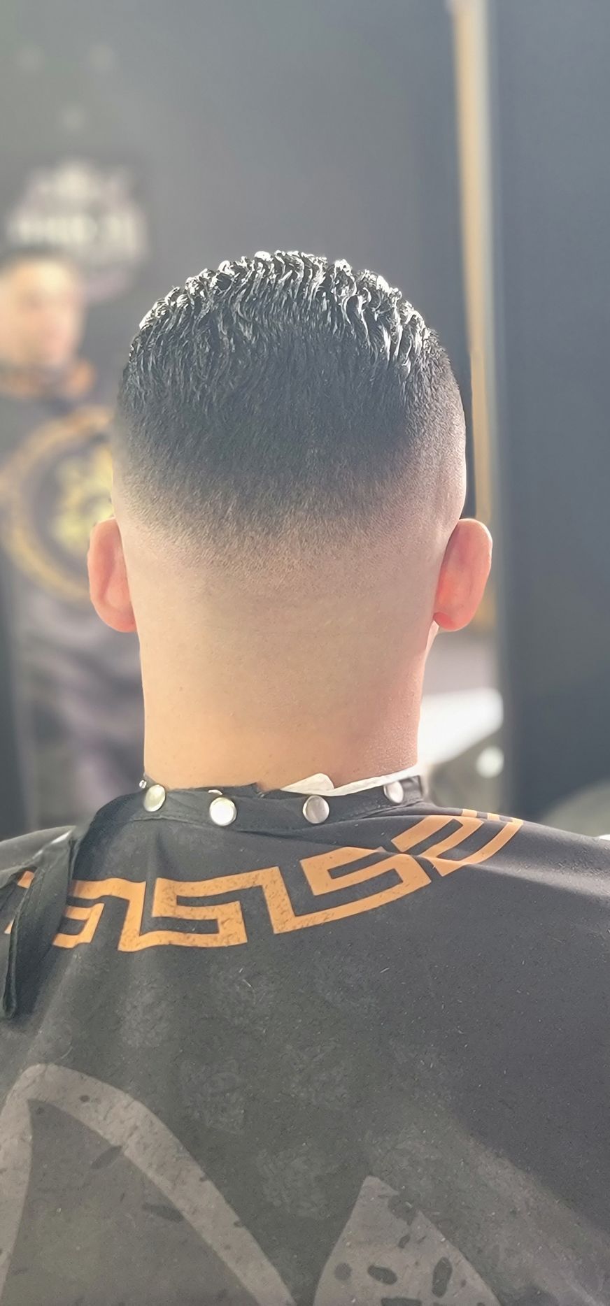 Man with a faded haircut in a barber shop, wearing a red cape.
