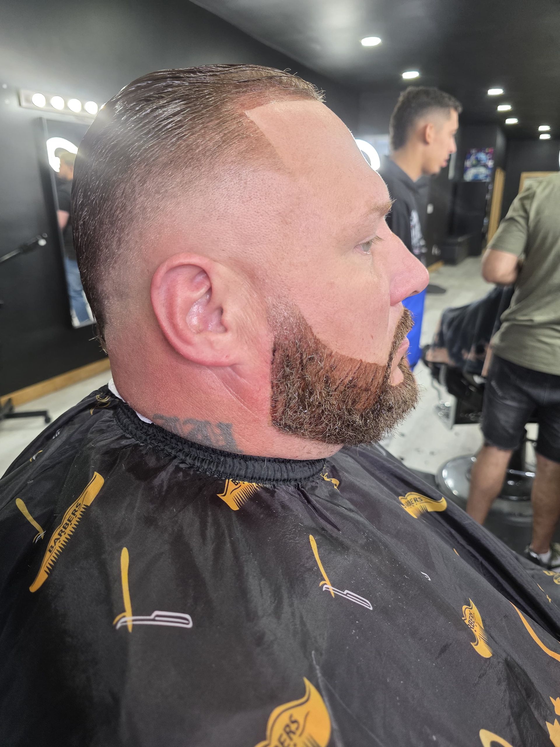 Man with a dark, shaped beard, short hair, and closed eyes in a salon.