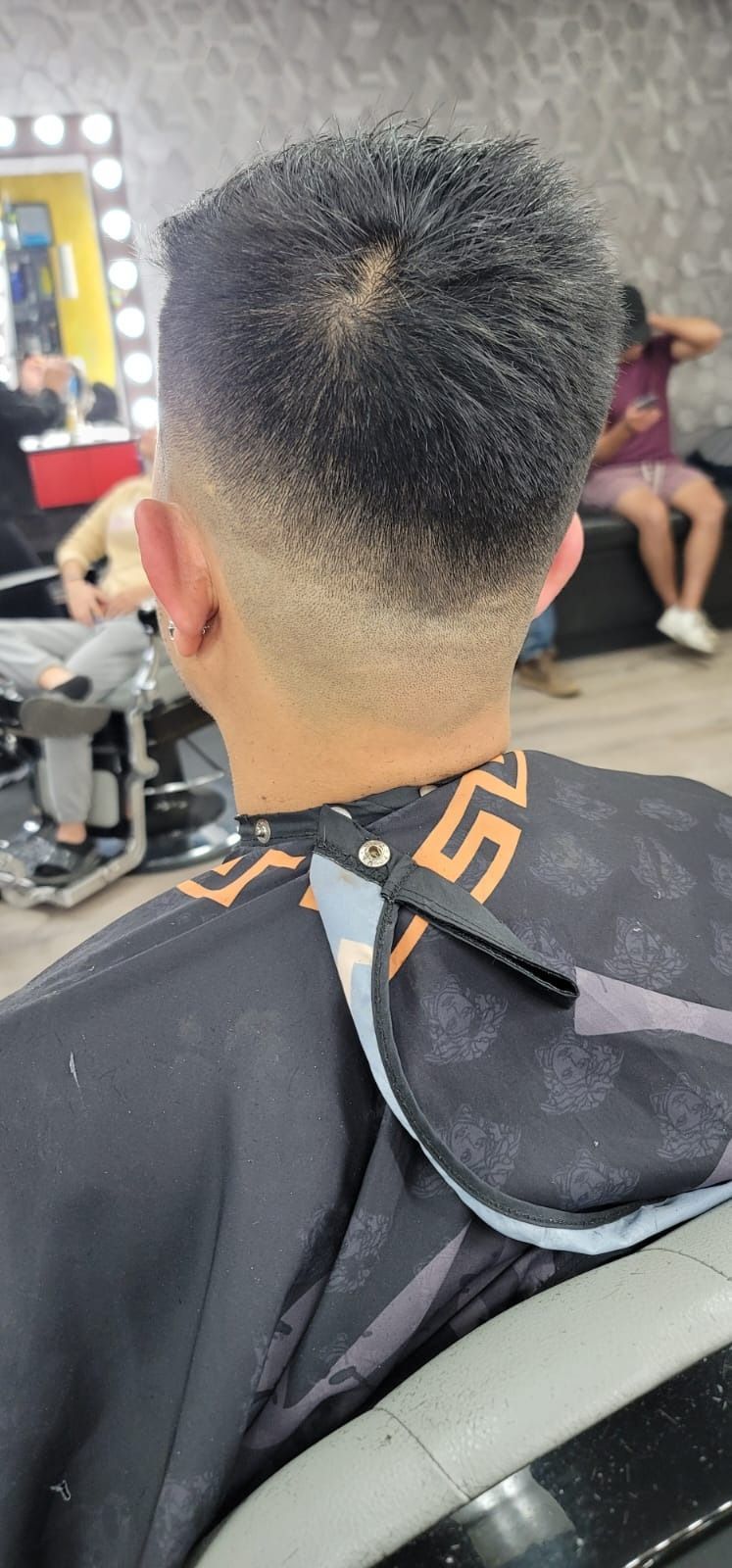 Man with a faded haircut at a barbershop, wearing a black cape.