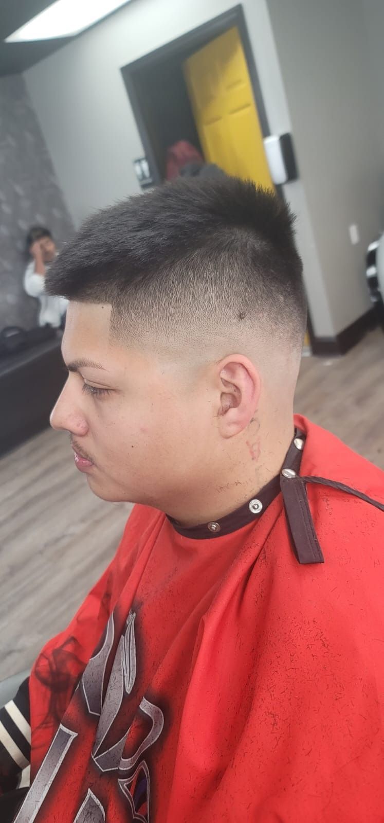 A young man with a fade haircut in a barber shop wearing a red cape.