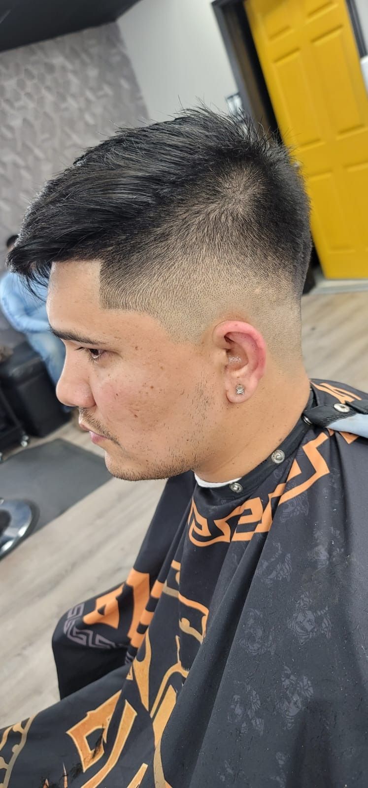 Man with a faded haircut at a barbershop, wearing a black cape.