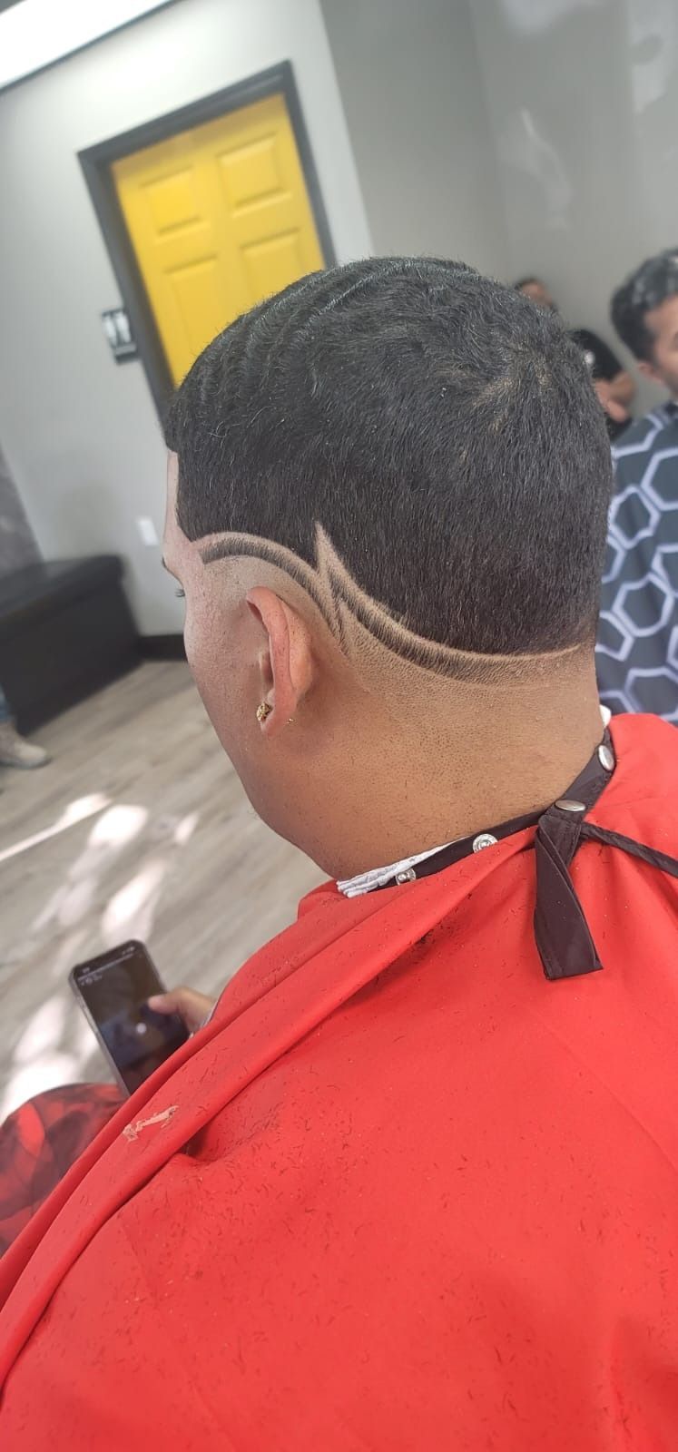 Person with a textured haircut and a design above the ear, in a barber shop.