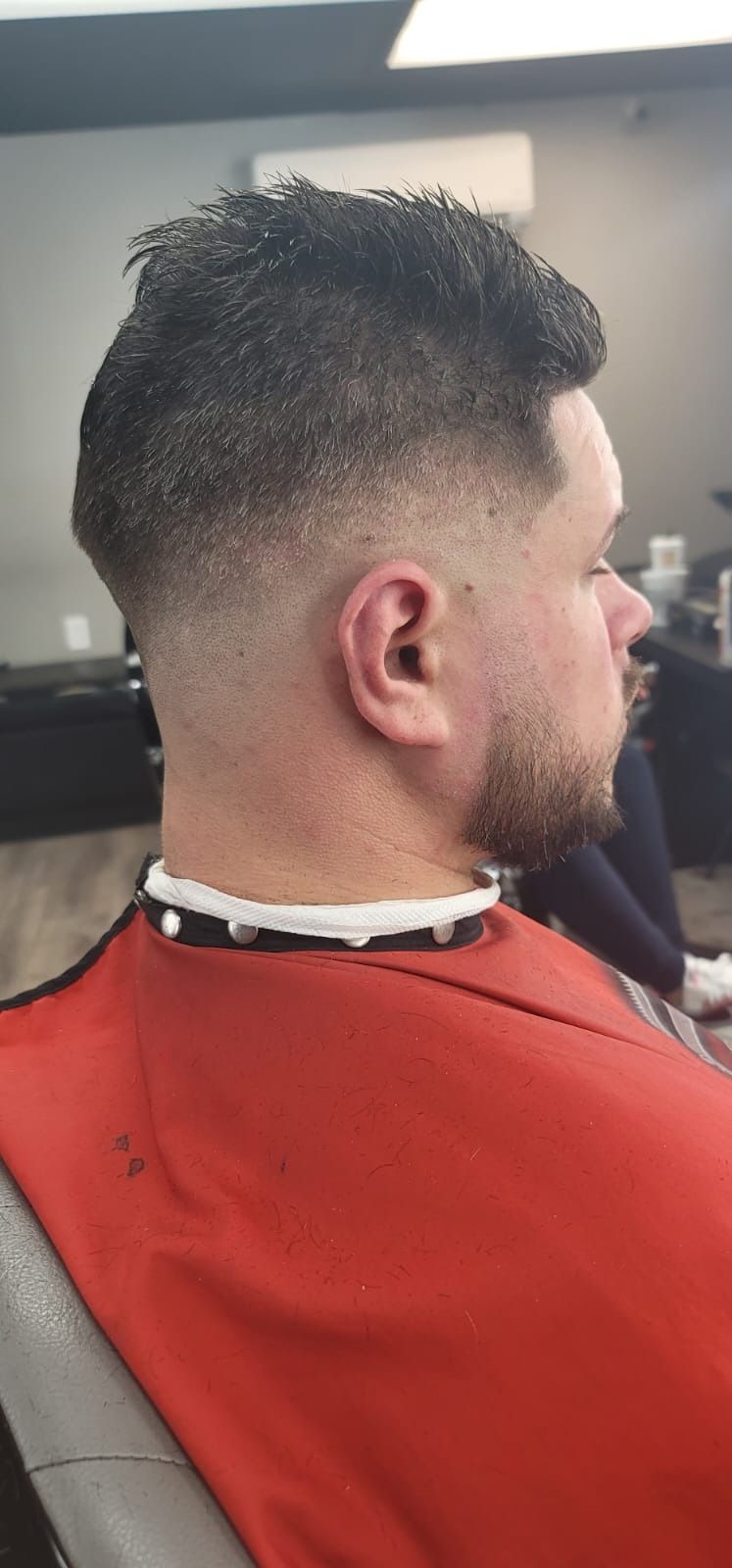 Man with a faded haircut in a barber shop, wearing a red cape.