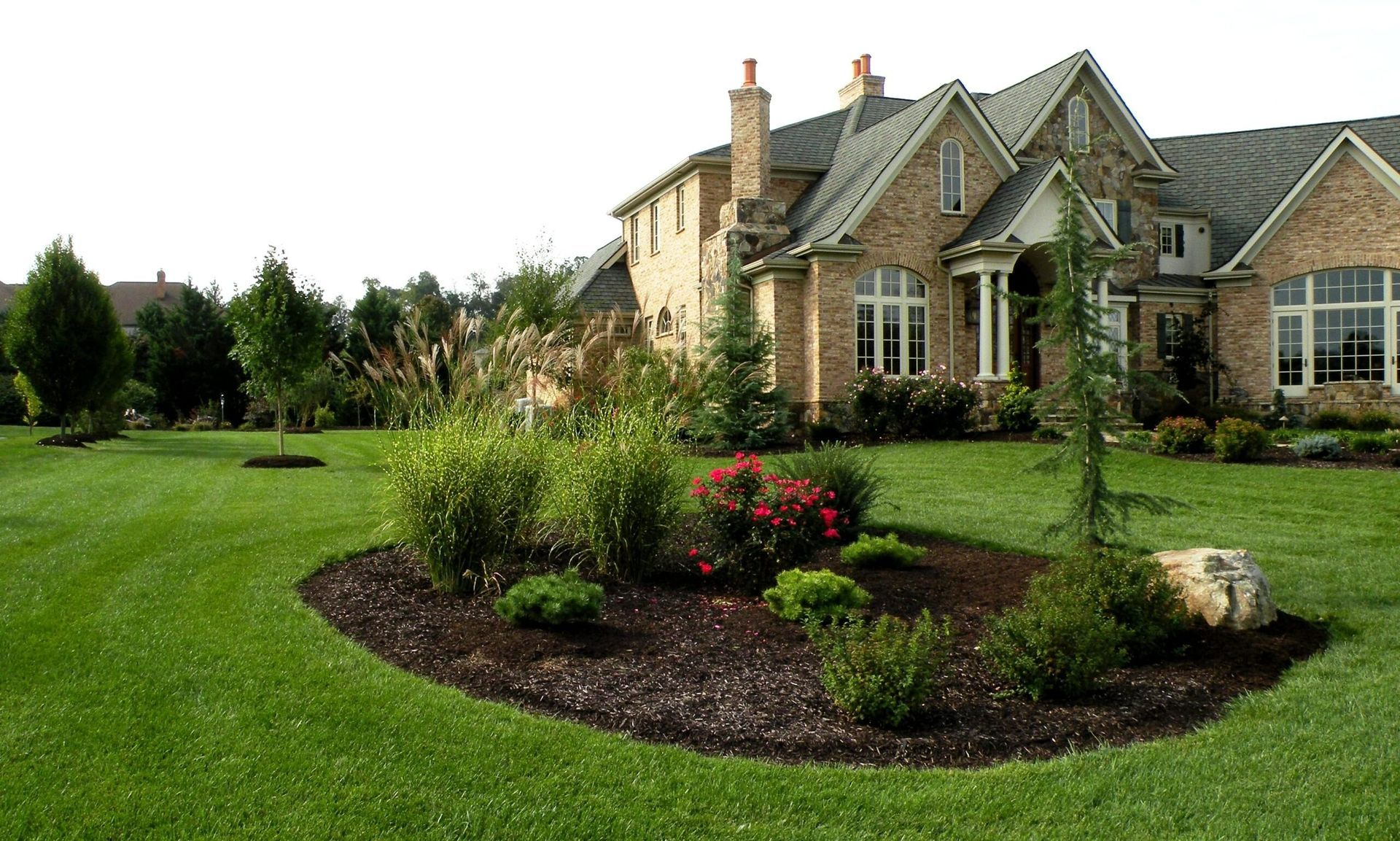 Large brick house with manicured lawn and flower bed.