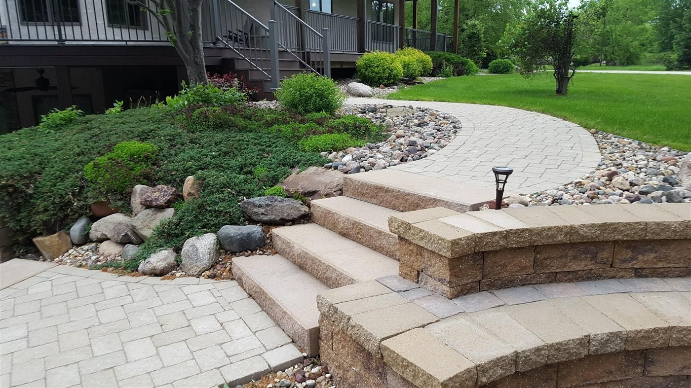 Stone walkway with steps leading to a house. Landscaping includes bushes, rocks and grass.