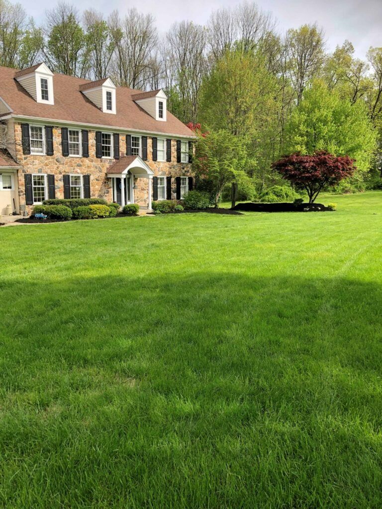 Two-story brick house with green lawn and trees under a cloudy sky.