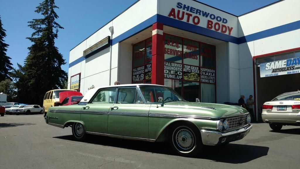 A green car is parked in front of sherwood auto body