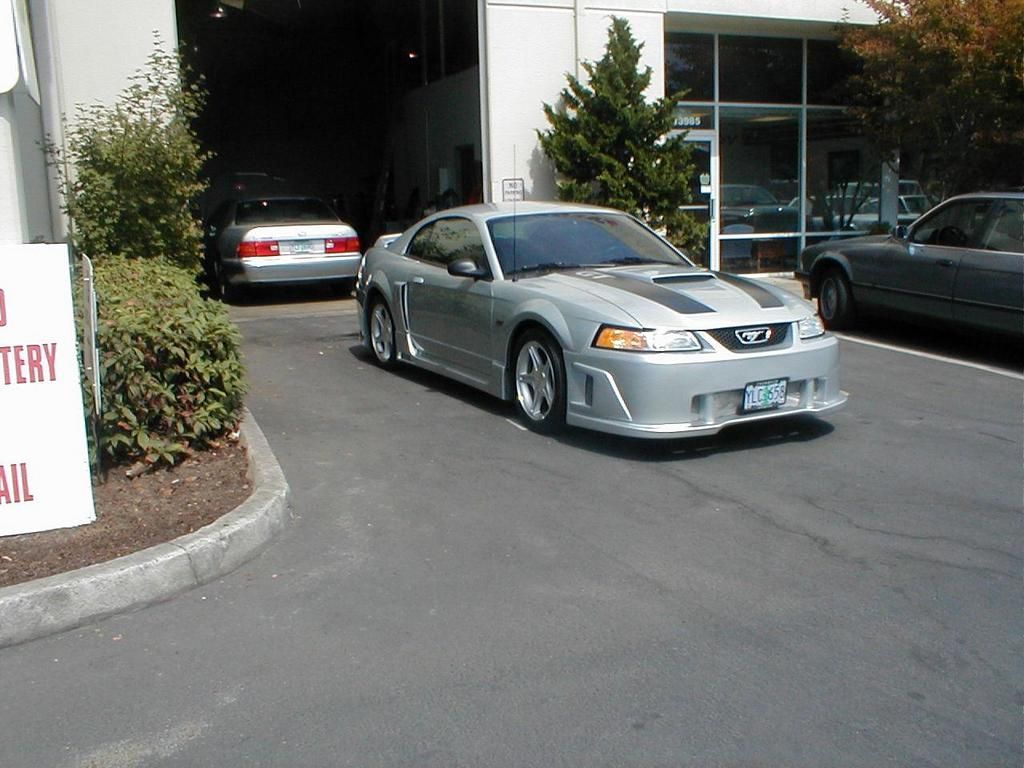 A silver mustang is parked in front of a building with a sign that says battery repair