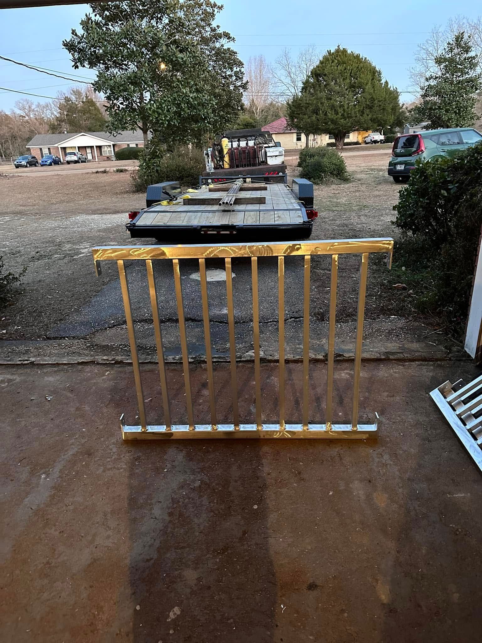 Gold-colored metal railing in front of a trailer on a gravel driveway, with trees and houses in the background.