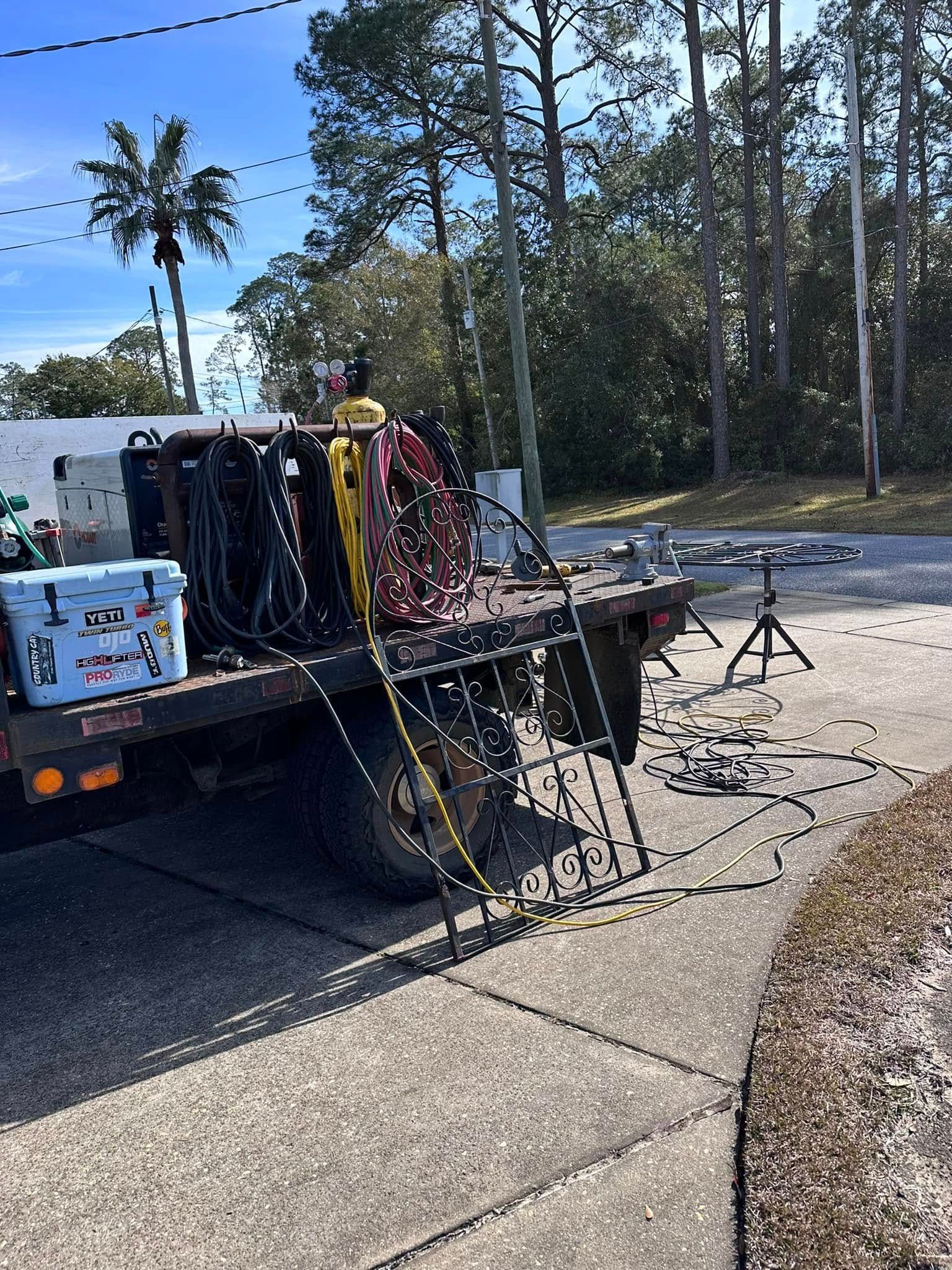 Flatbed truck with equipment; hoses, tanks, cooler, and ladder on a concrete driveway. Trees in the background.