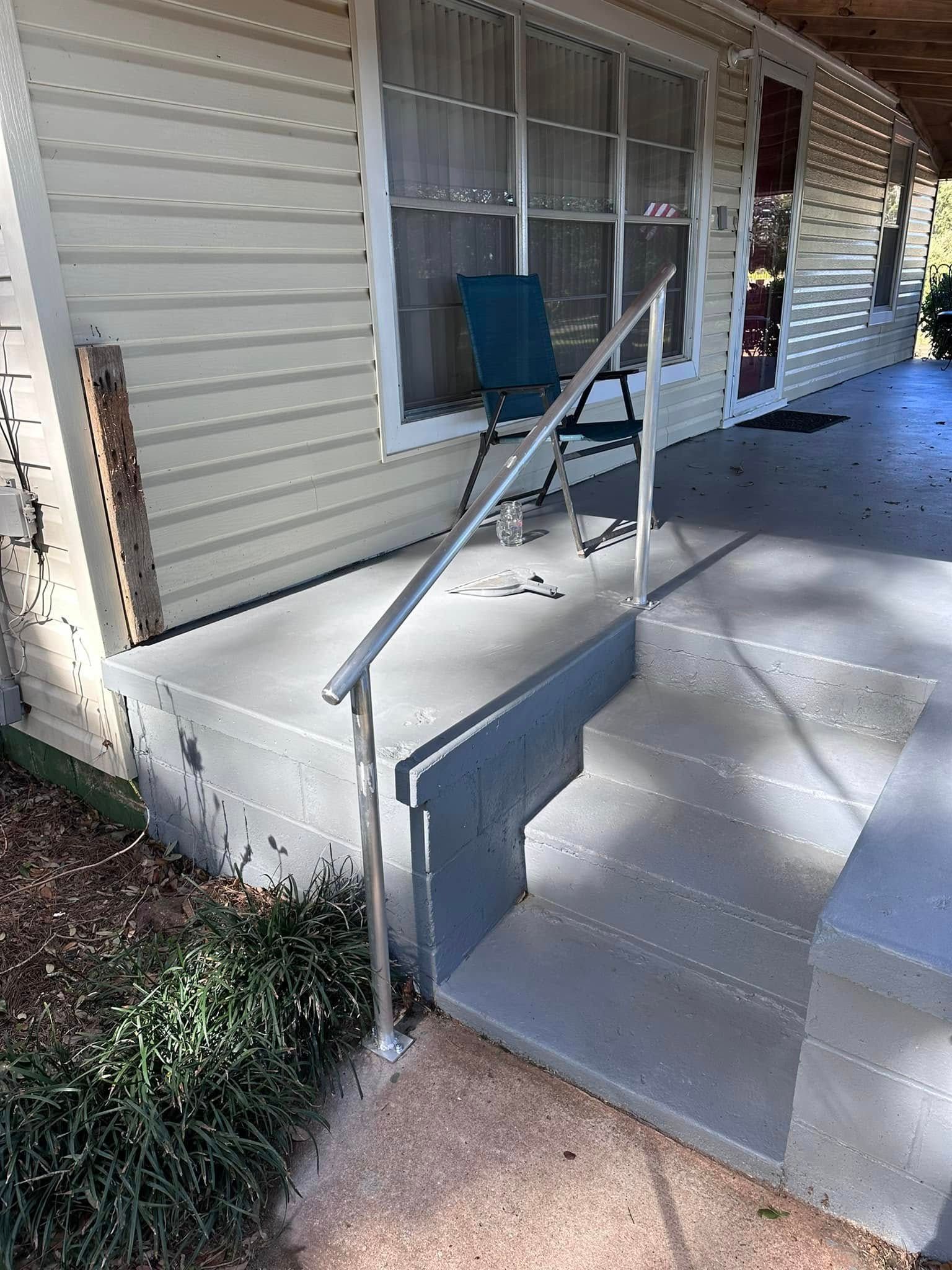 Exterior view of house porch with steps and handrail, gray painted concrete, and a blue chair.