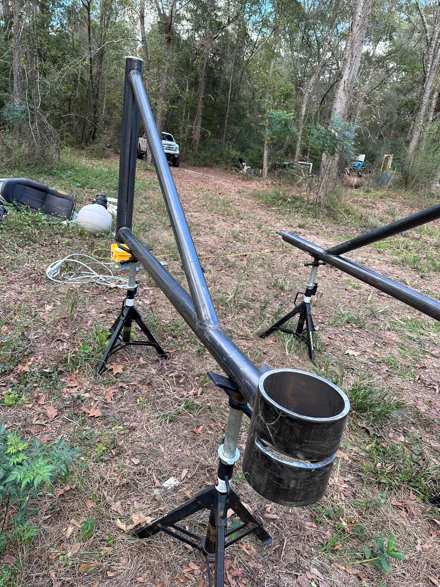 Metal contraption supported by tripods outdoors; possibly for filming or other equipment.