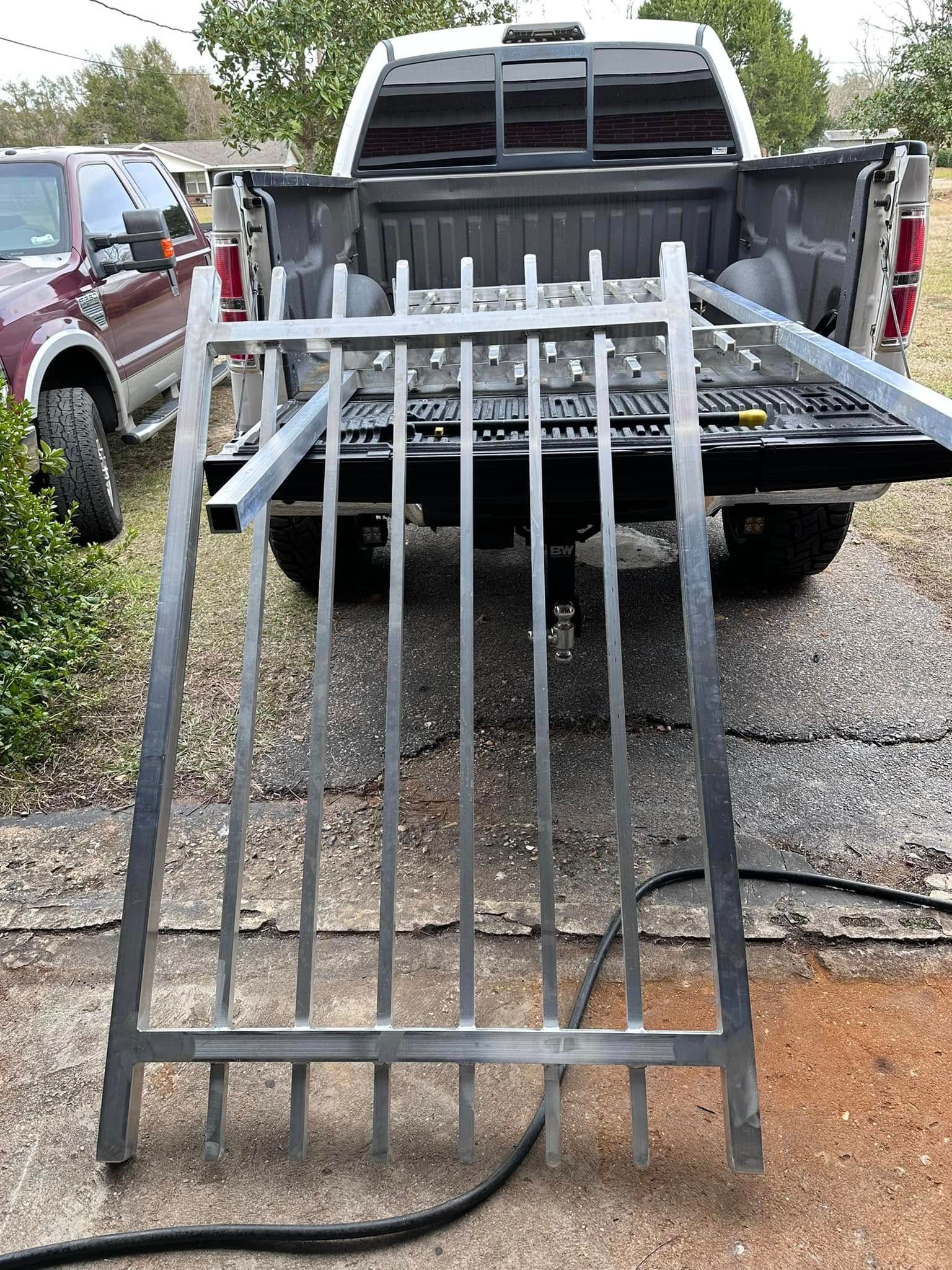 Metal ramp leaning against the open bed of a white pickup truck.
