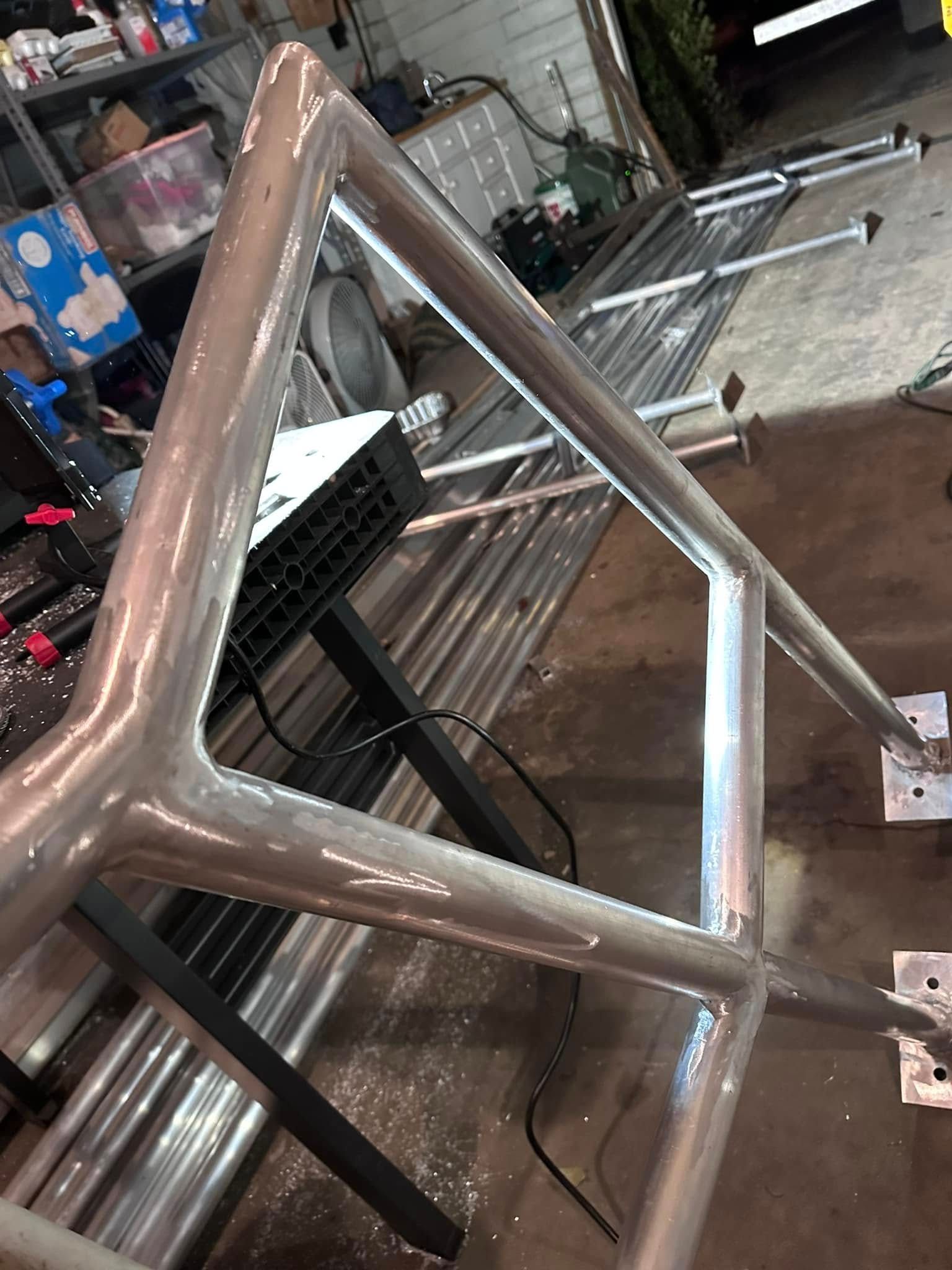 Welded metal frame, triangular shape, mounted on metal plates. Workshop background.