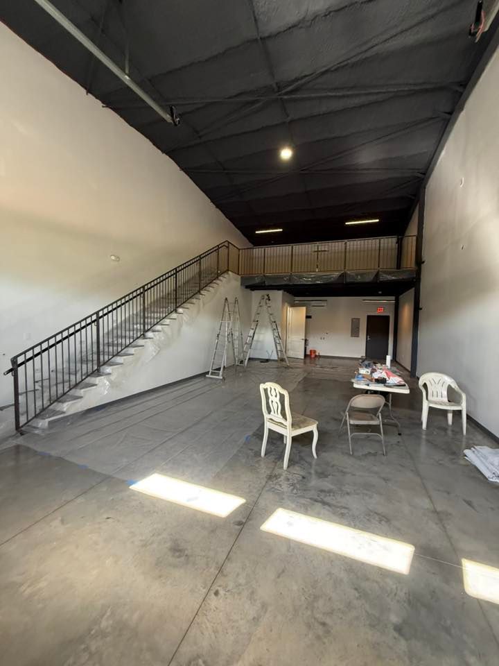 Empty warehouse interior with stairs, a mezzanine, and a few chairs.