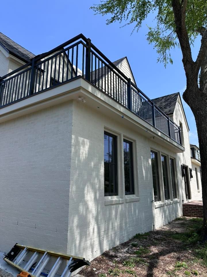 White brick building with black balcony railing, windows, and ladder on a sunny day.