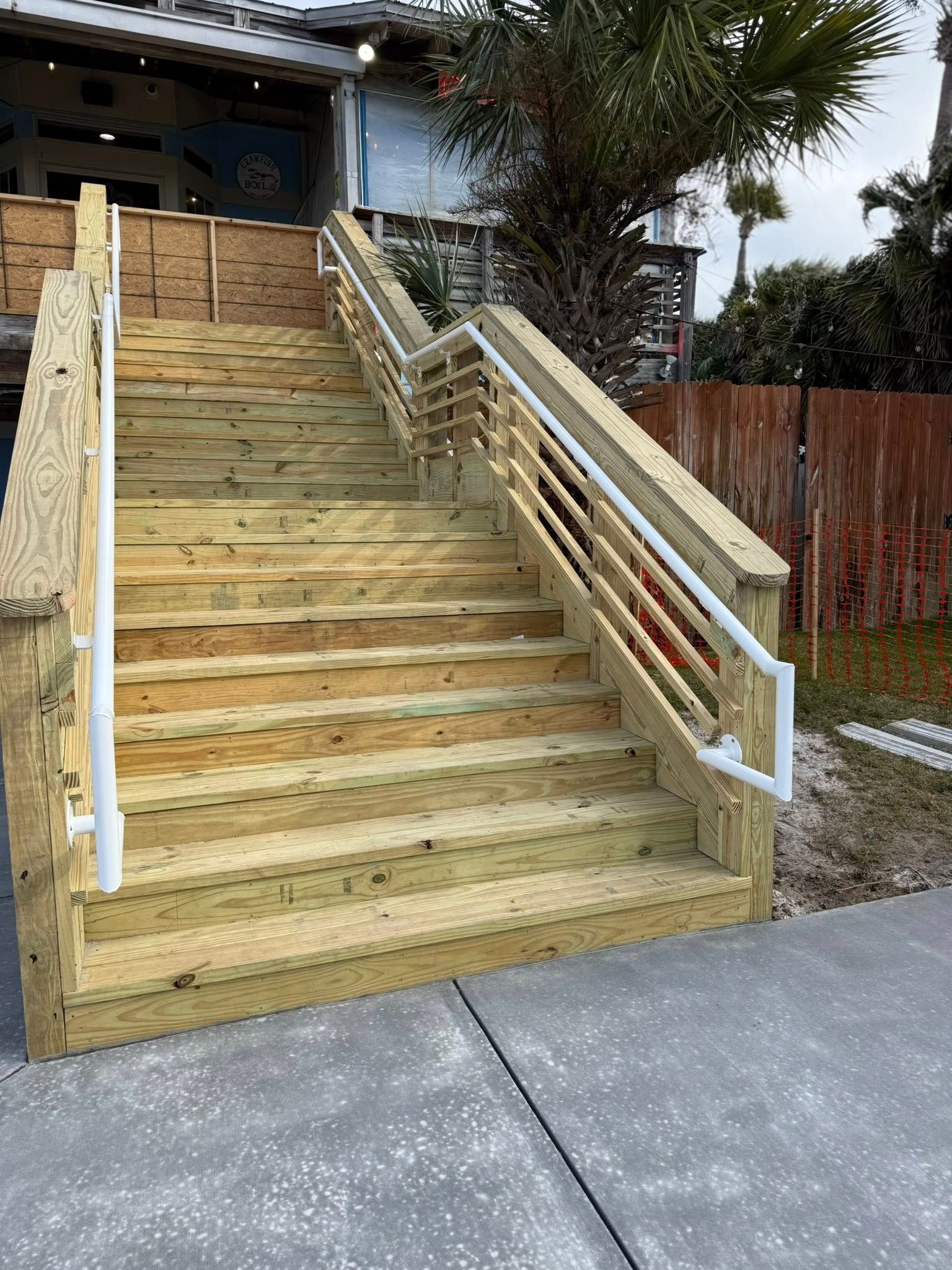 Wooden outdoor stairs with white handrails leading to a building entrance.