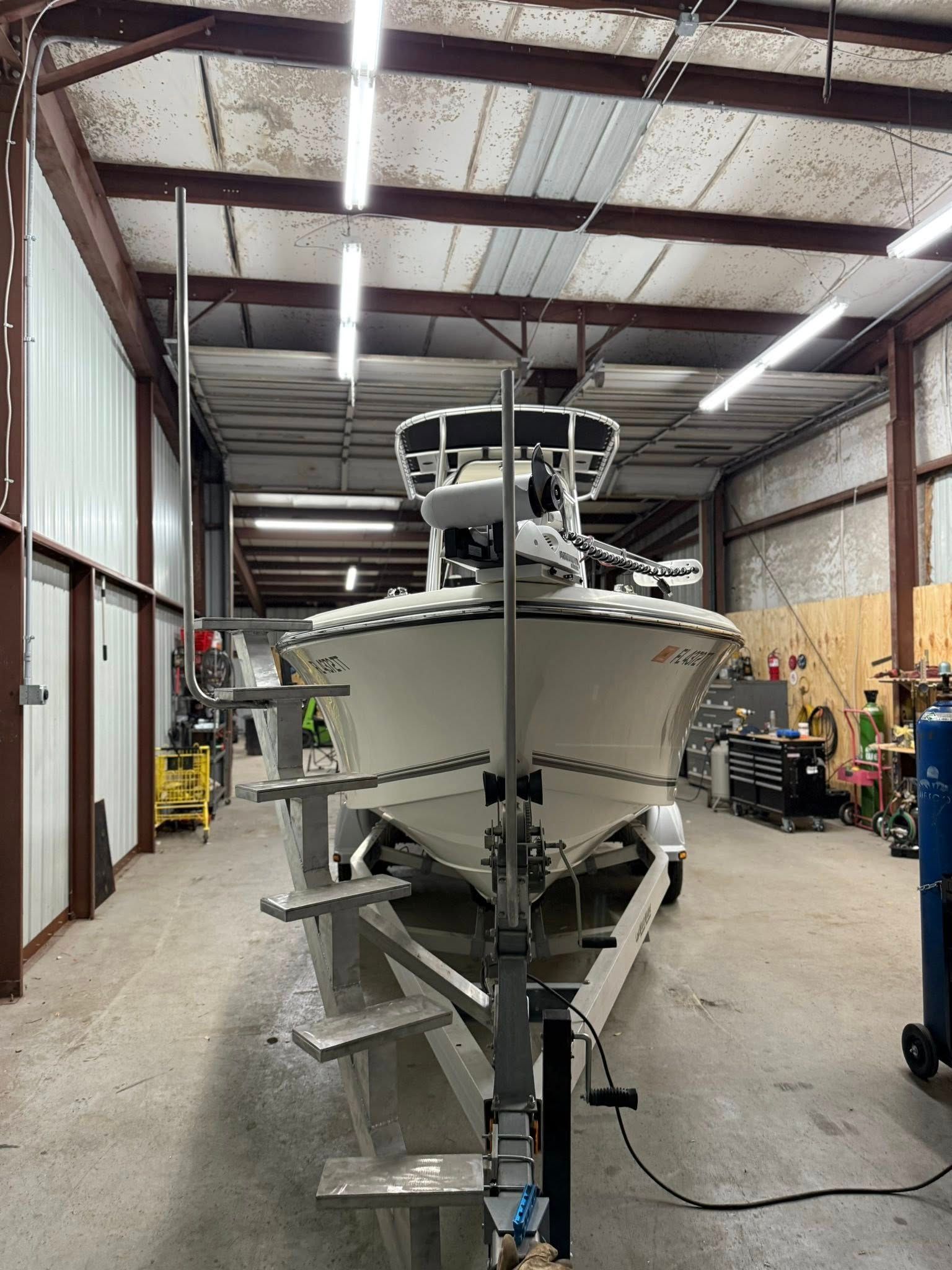Boat on trailer inside a workshop, with metal supports and overhead lighting.