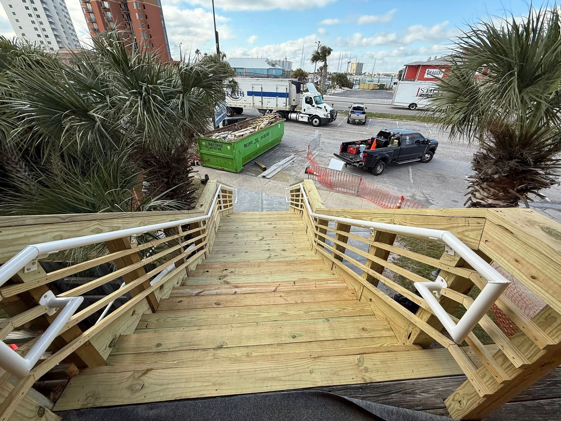 Wooden staircase leads down to a construction site with vehicles and a green dumpster.