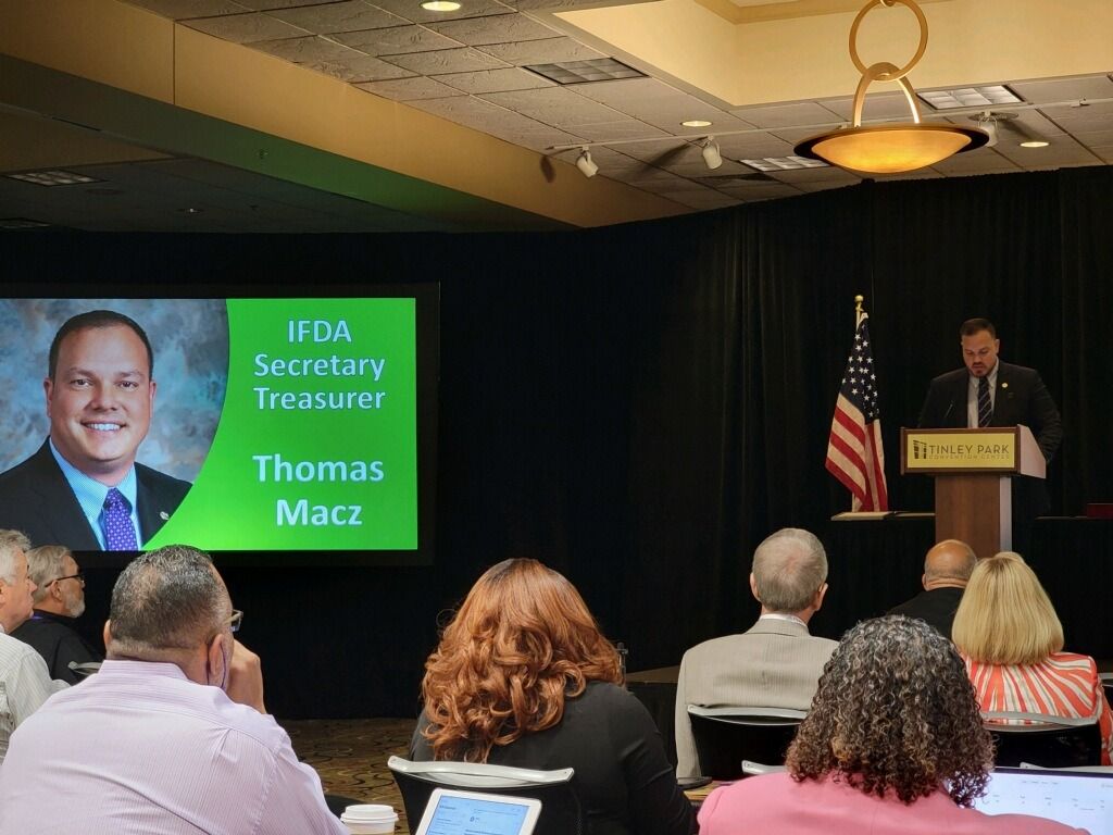 Man speaking at a podium with a screen displaying 