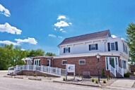 Two-story white building with red brick, ramp, and blue sky.