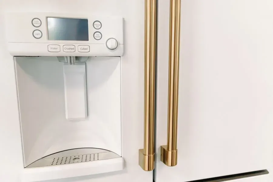 A white refrigerator with gold handles and a water dispenser on the door.