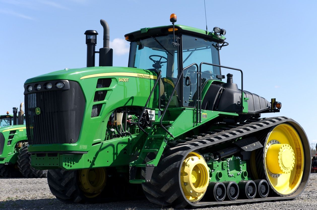 Green agricultural tractor with large yellow wheels on a gravel lot under a blue sky