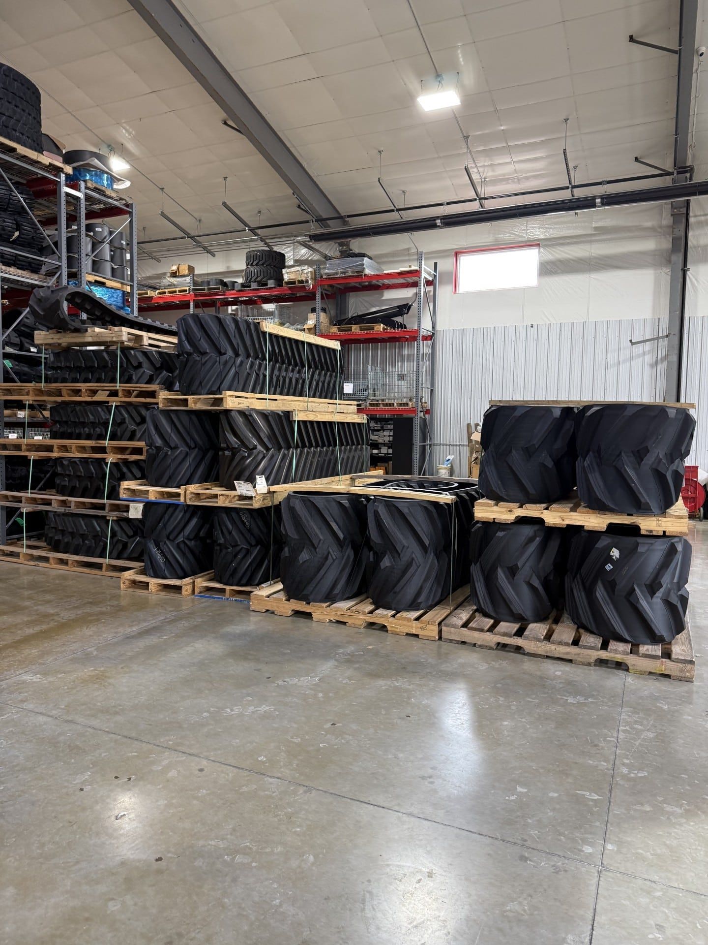 Warehouse aisle with stacked black-wrapped pallets and shelving on a polished concrete floor.