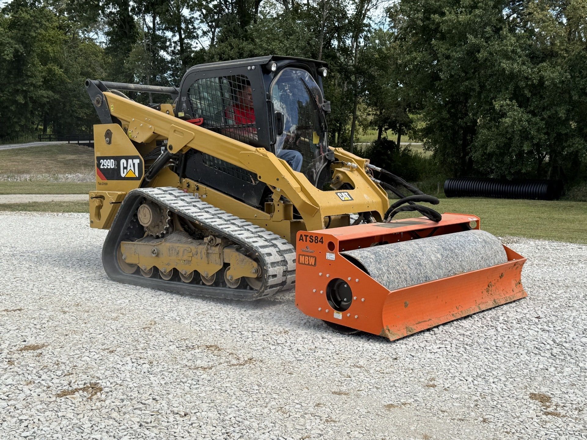 Yellow Caterpillar skid steer with orange brush mower attachment on gravel outdoors.