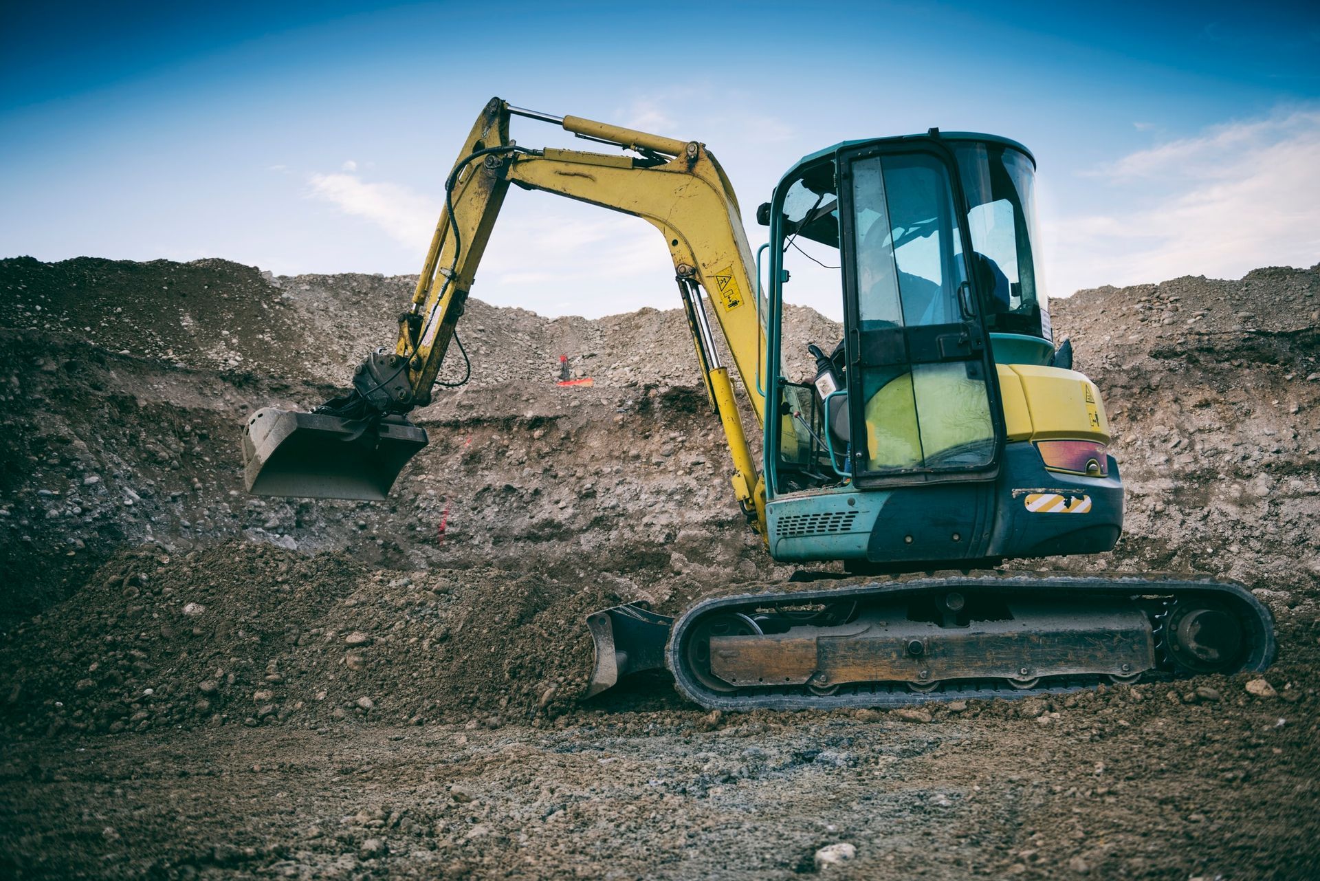 Yellow excavator working on a dirt mound at a construction site under a clear sky