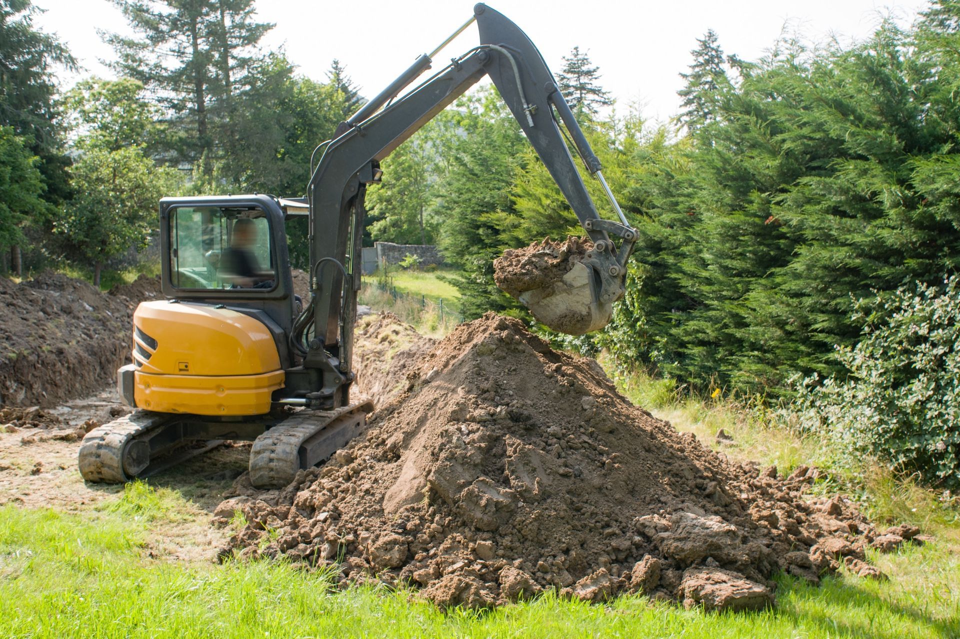 Yellow excavator digging a dirt pile at a wooded construction site