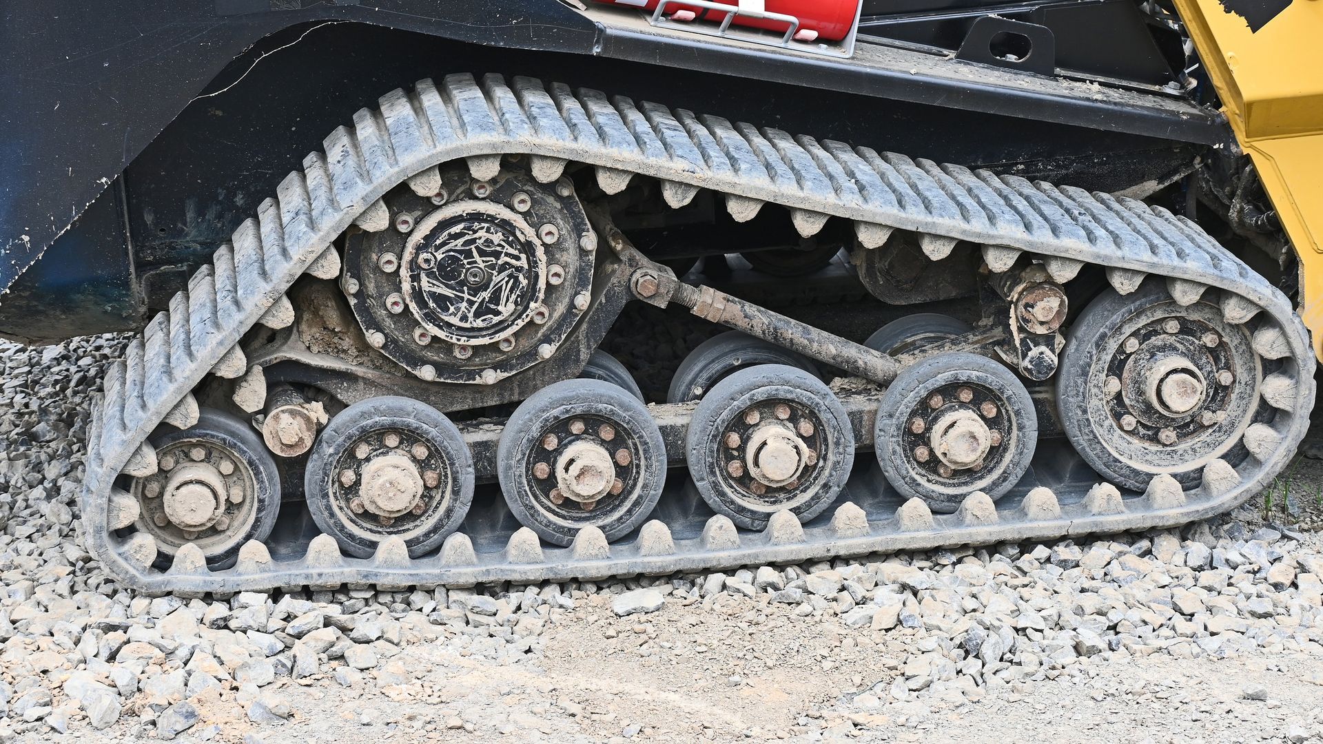 Close-up of a black tracked vehicle’s undercarriage on gravel, showing wheels and treads.