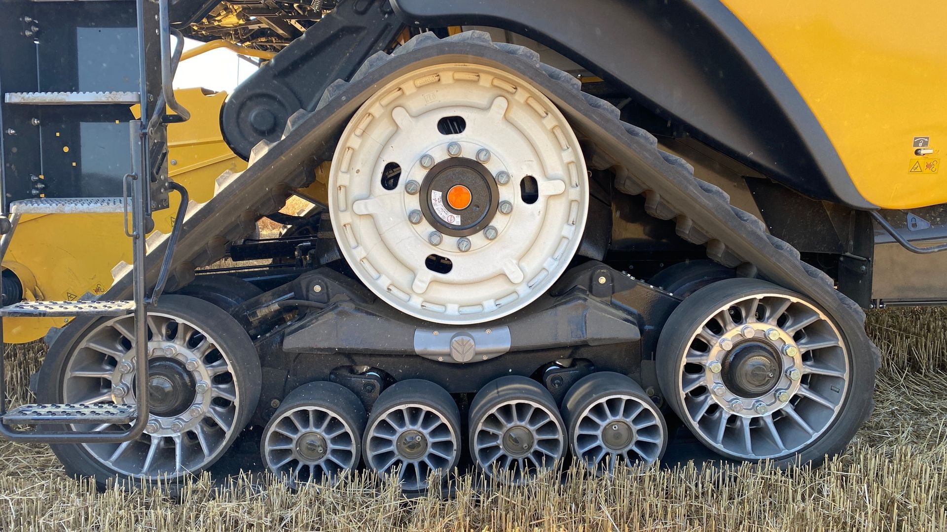 Close-up of a yellow tracked machine’s undercarriage with metal wheels on dry grass.