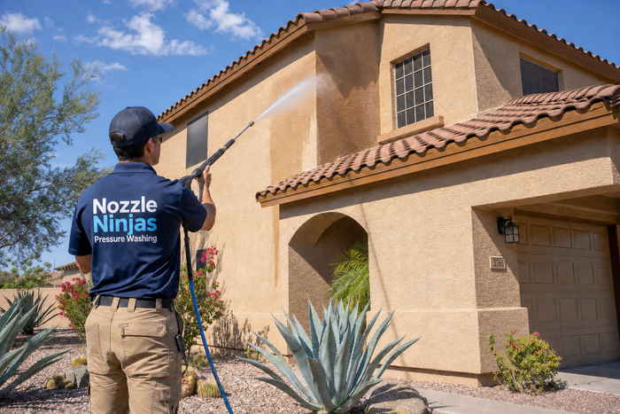 Technician in Nozzle Ninjas shirt spraying stucco house exterior with a pressure washer