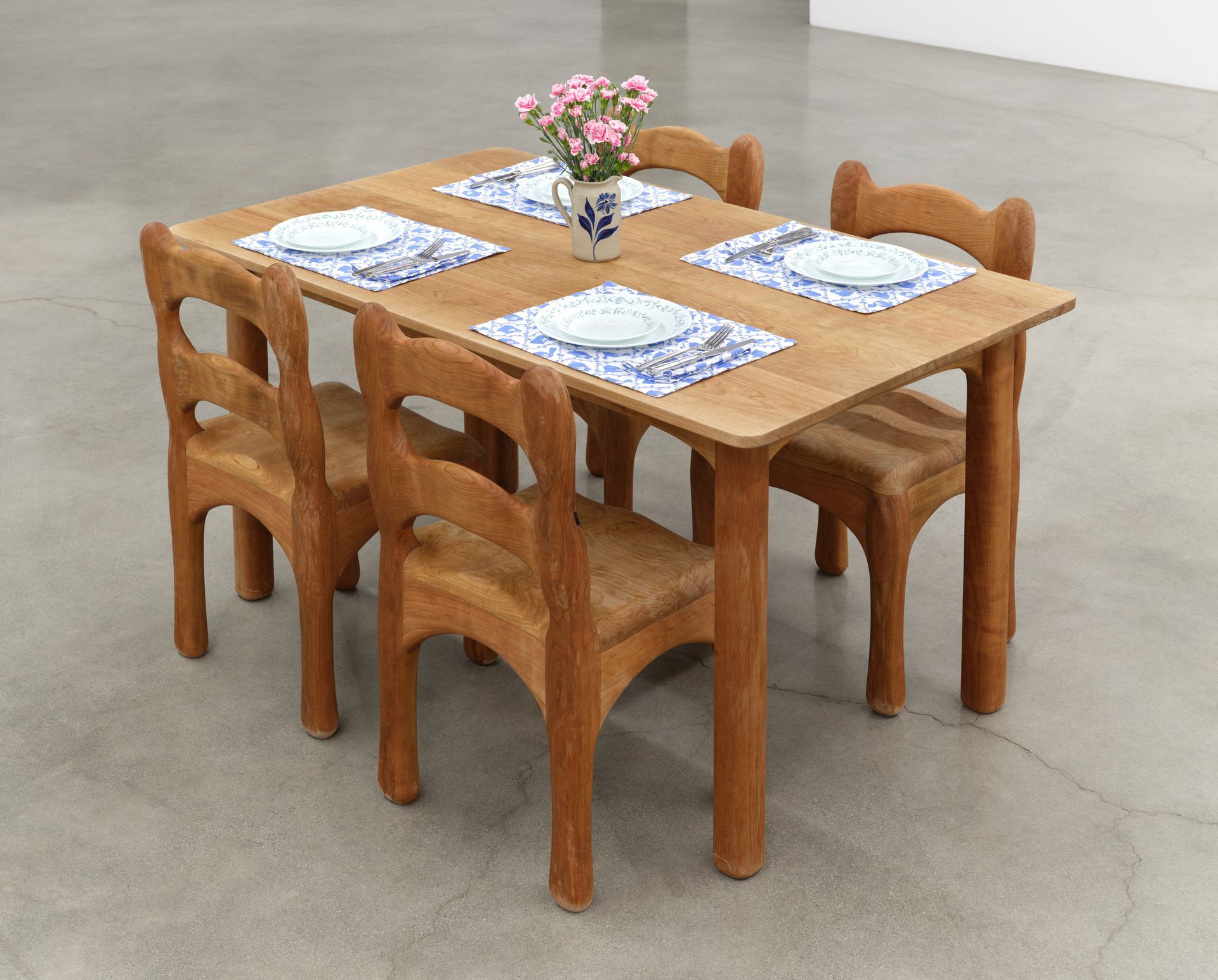 A wooden dining set: table with four chairs, set with placemats, plates, and a vase of flowers.