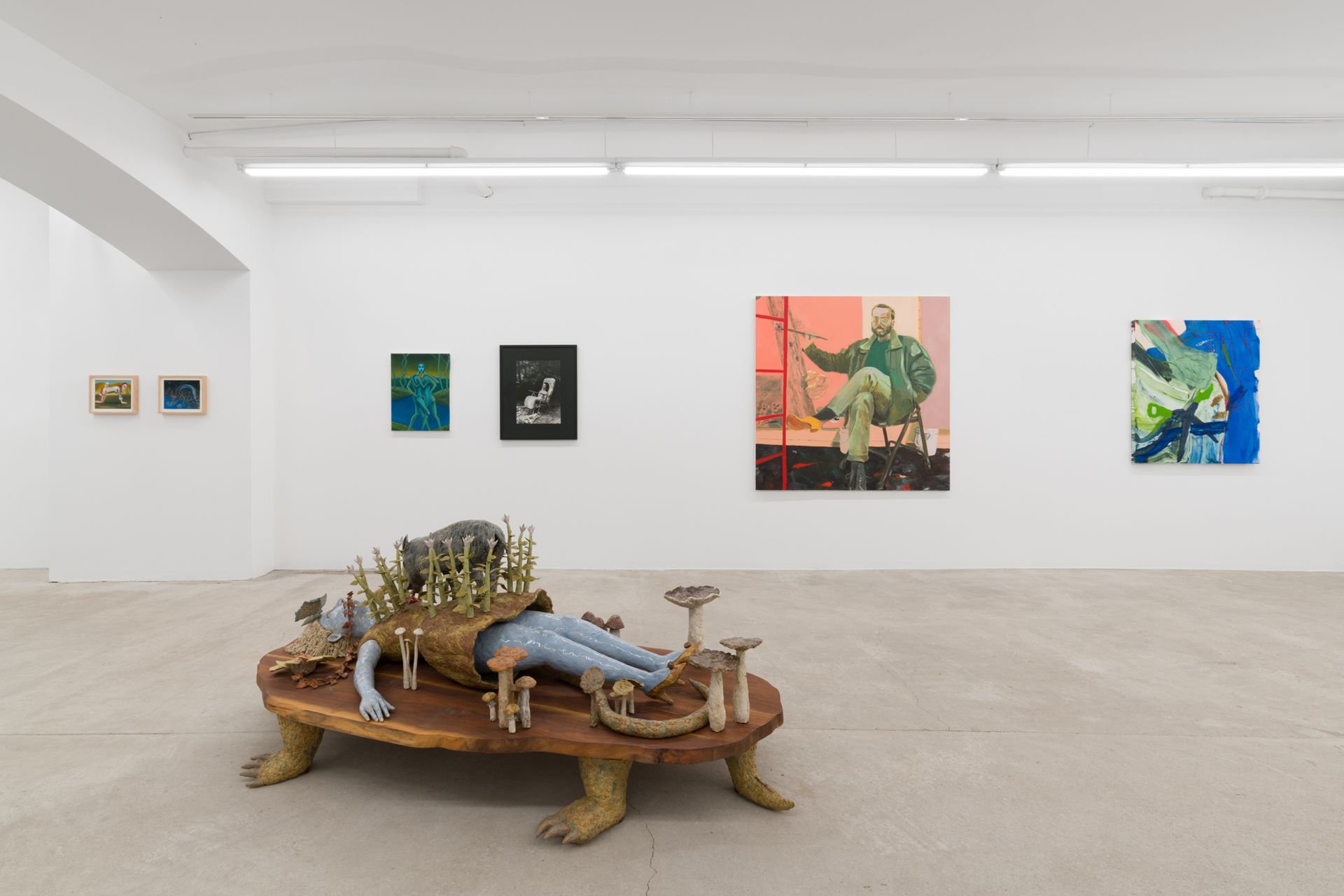 Art gallery with sculpture of reclining figure on turtle base and paintings on walls.