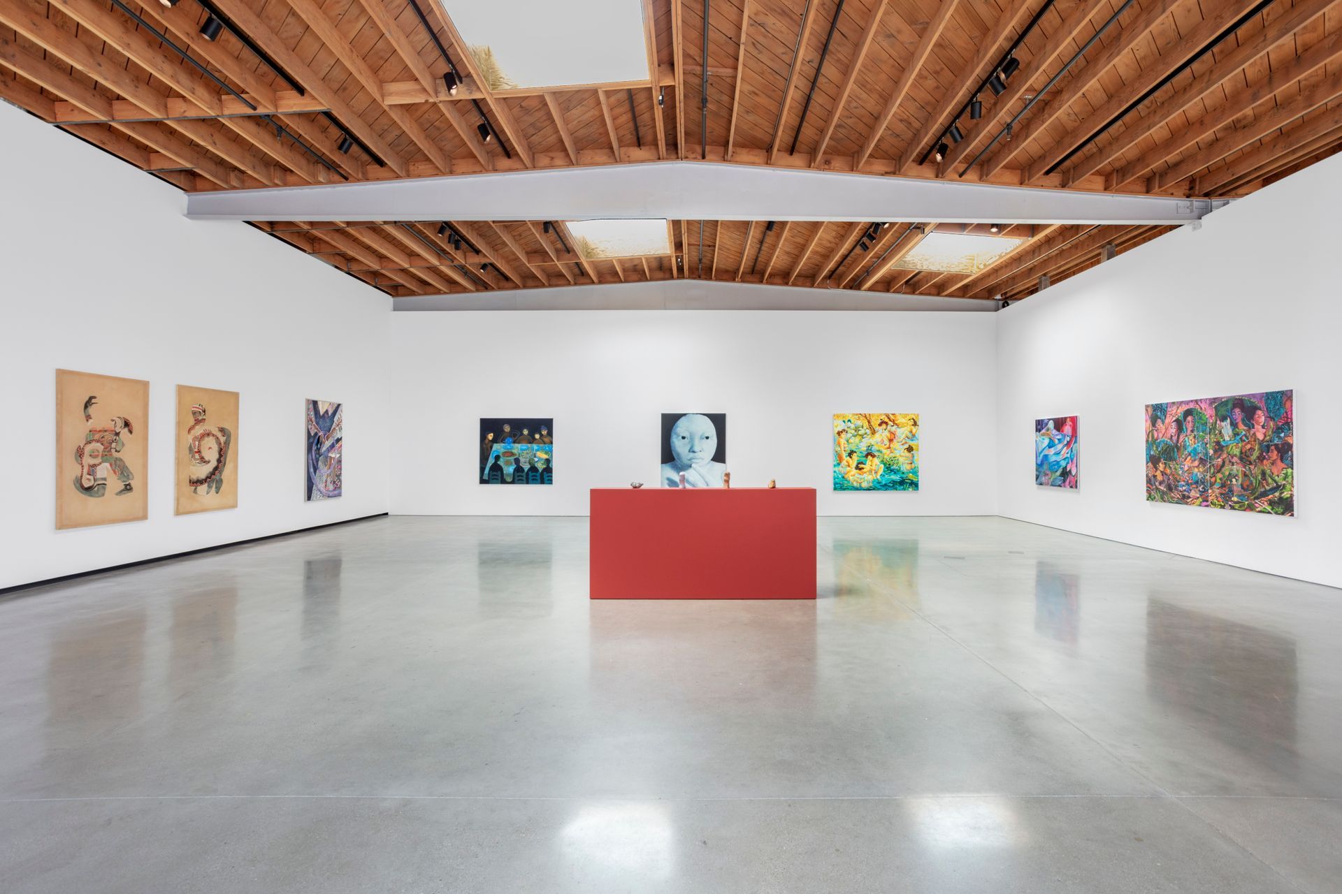 Art gallery with paintings displayed on white walls, red centerpiece, and a wood ceiling.