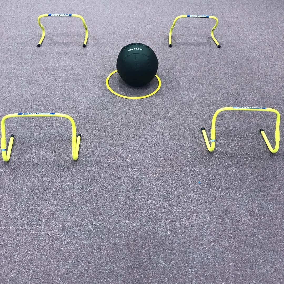 Yellow hurdles surround a dark green ball and a yellow hoop on a gray carpet.