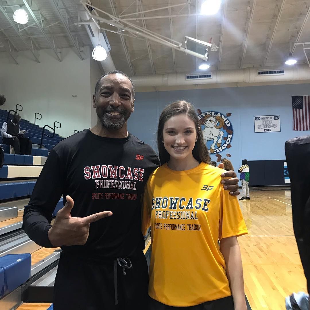 A man and a young woman pose together indoors at a basketball court. They both wear 