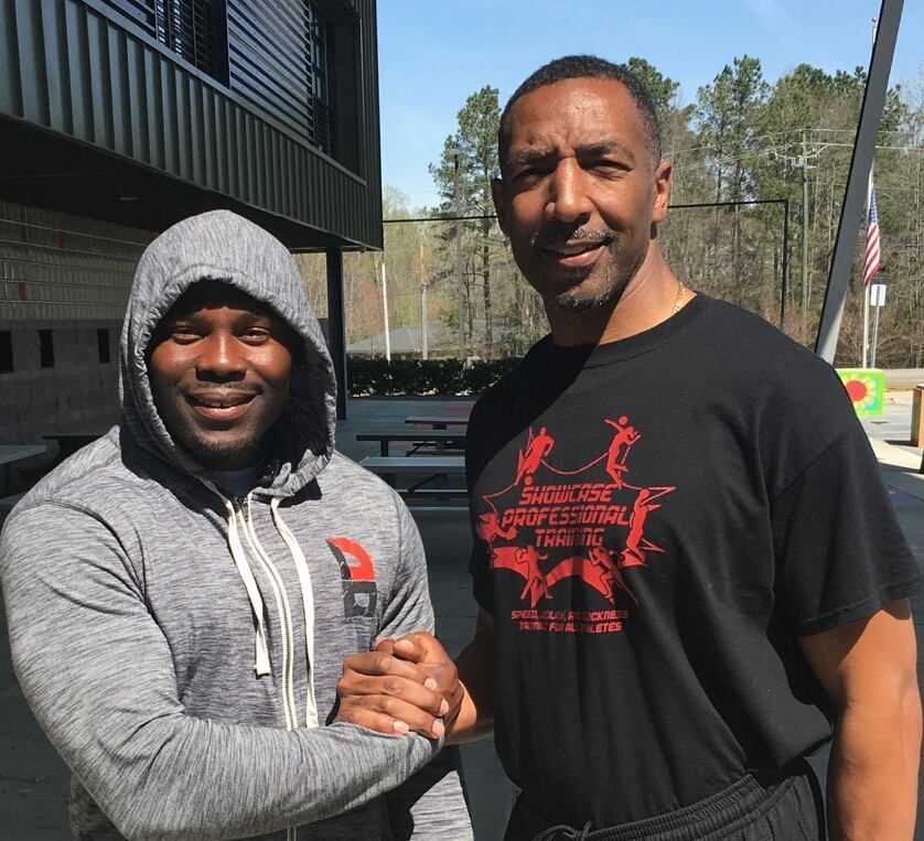 Two men shaking hands outdoors, one wearing a gray hoodie, the other a black t-shirt.