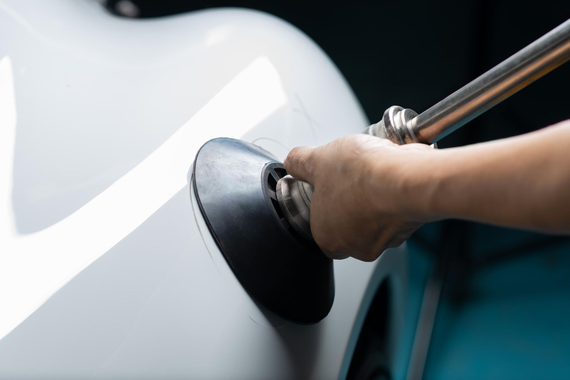 A hand using a dent puller tool on a white car to remove a dent.