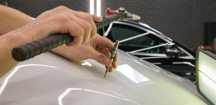 A person uses a tool to remove a dent from a car hood.