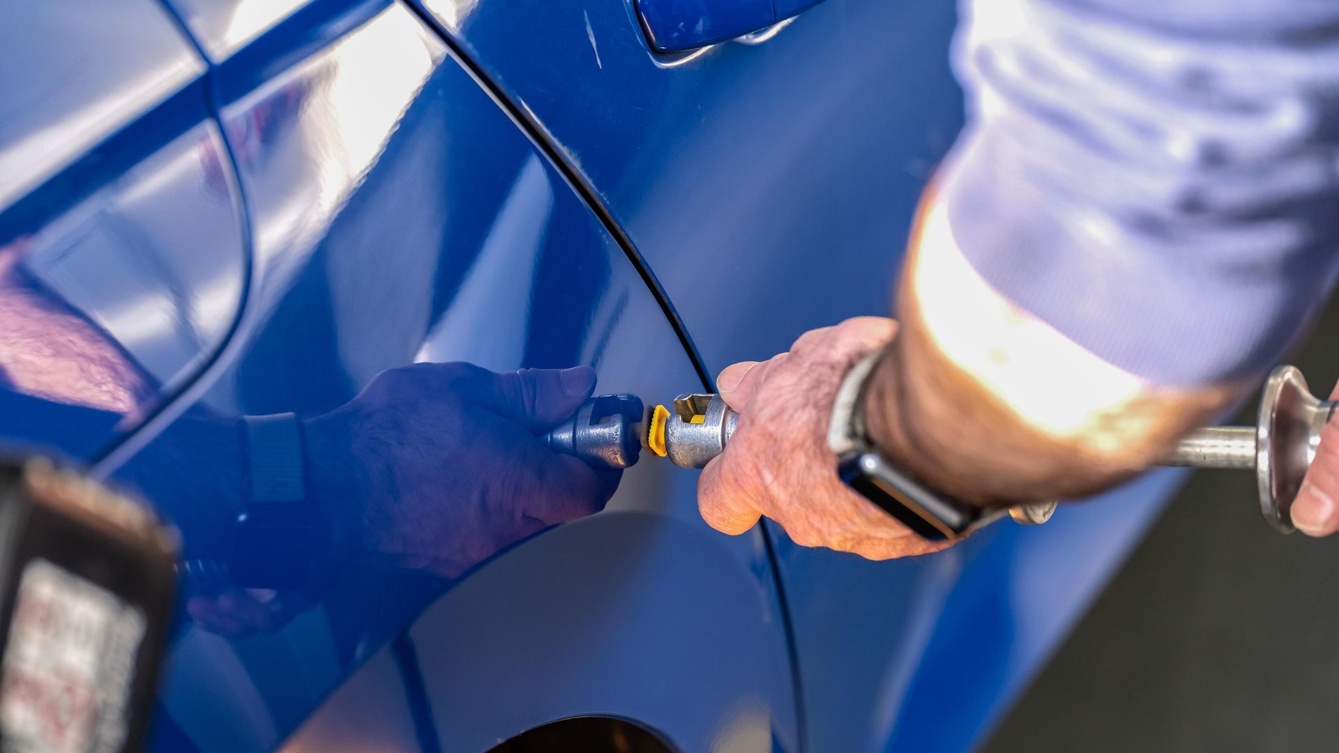 Person using a tool to repair a dent on a blue car.