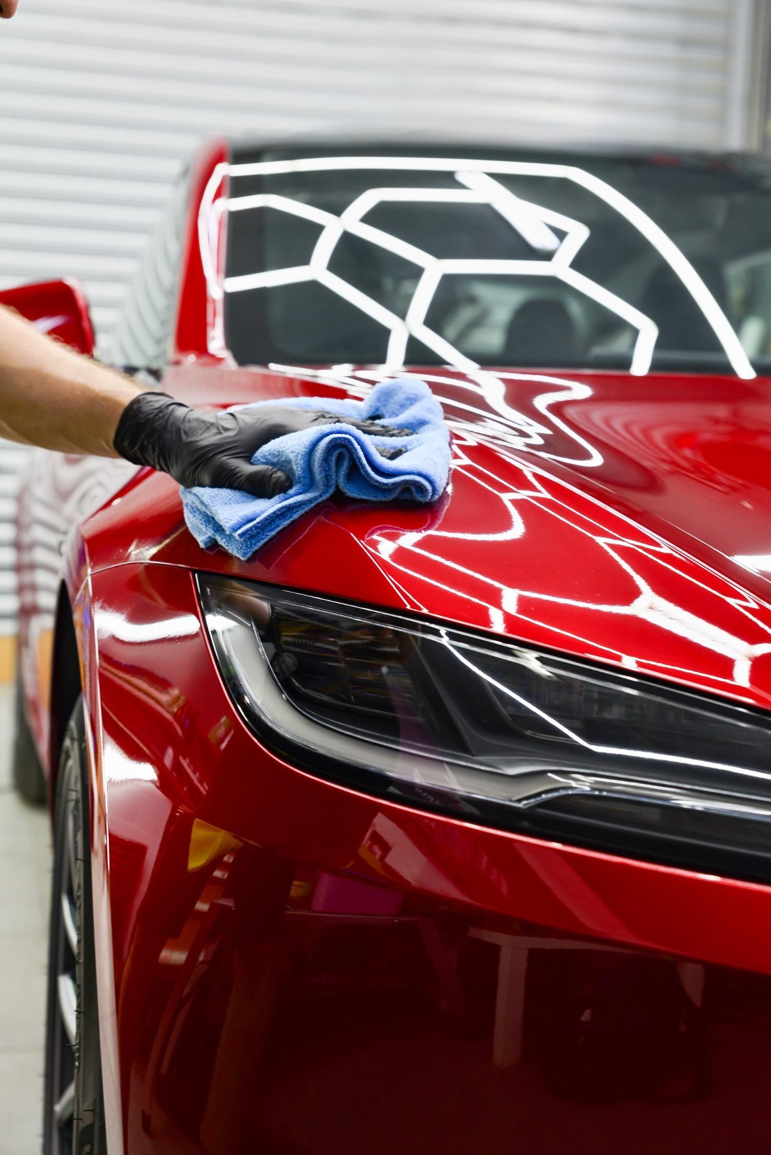 Person in black gloves wiping a shiny red car with a blue cloth.
