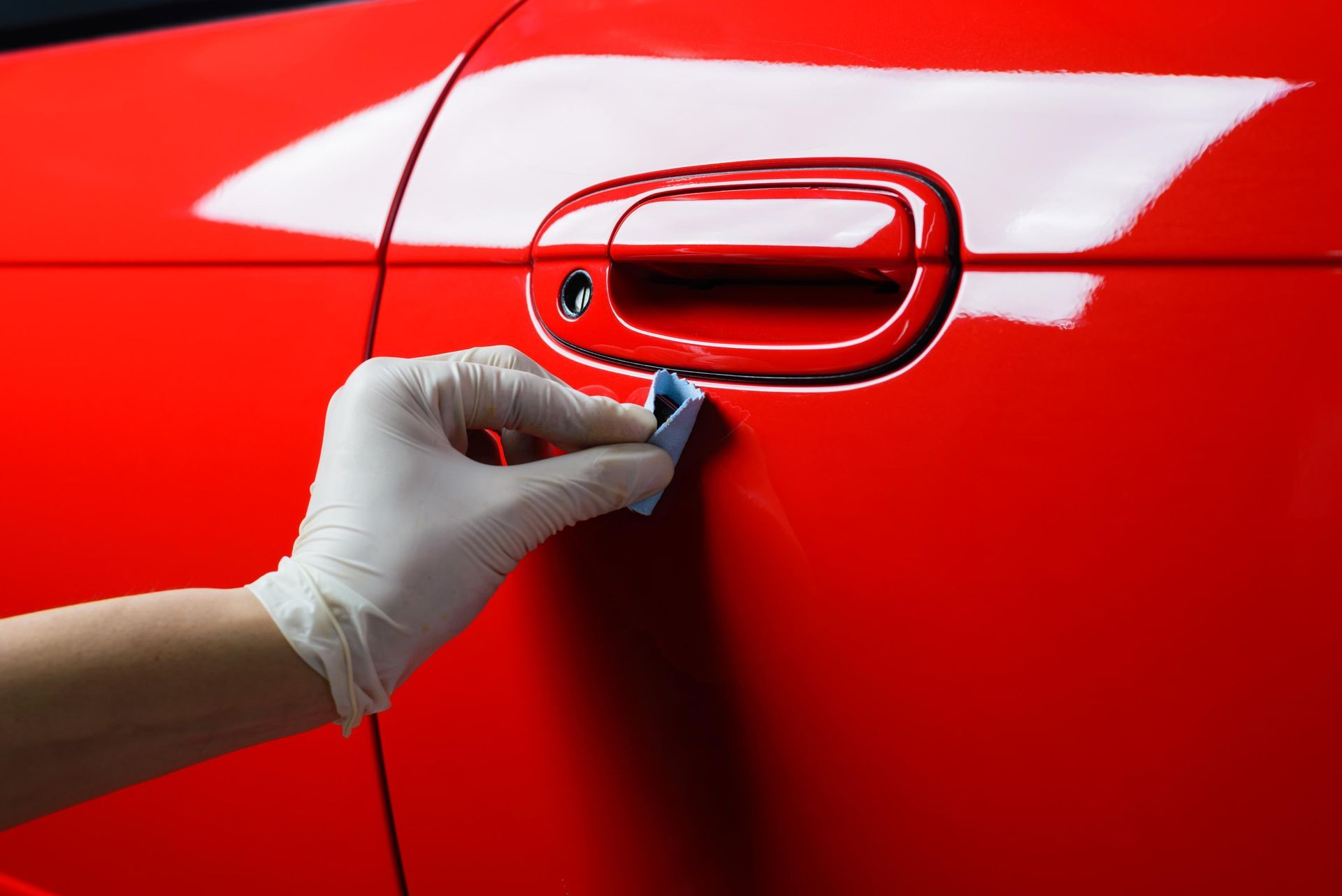Gloved hand applying a ceramic coating to a red car door, near the handle.