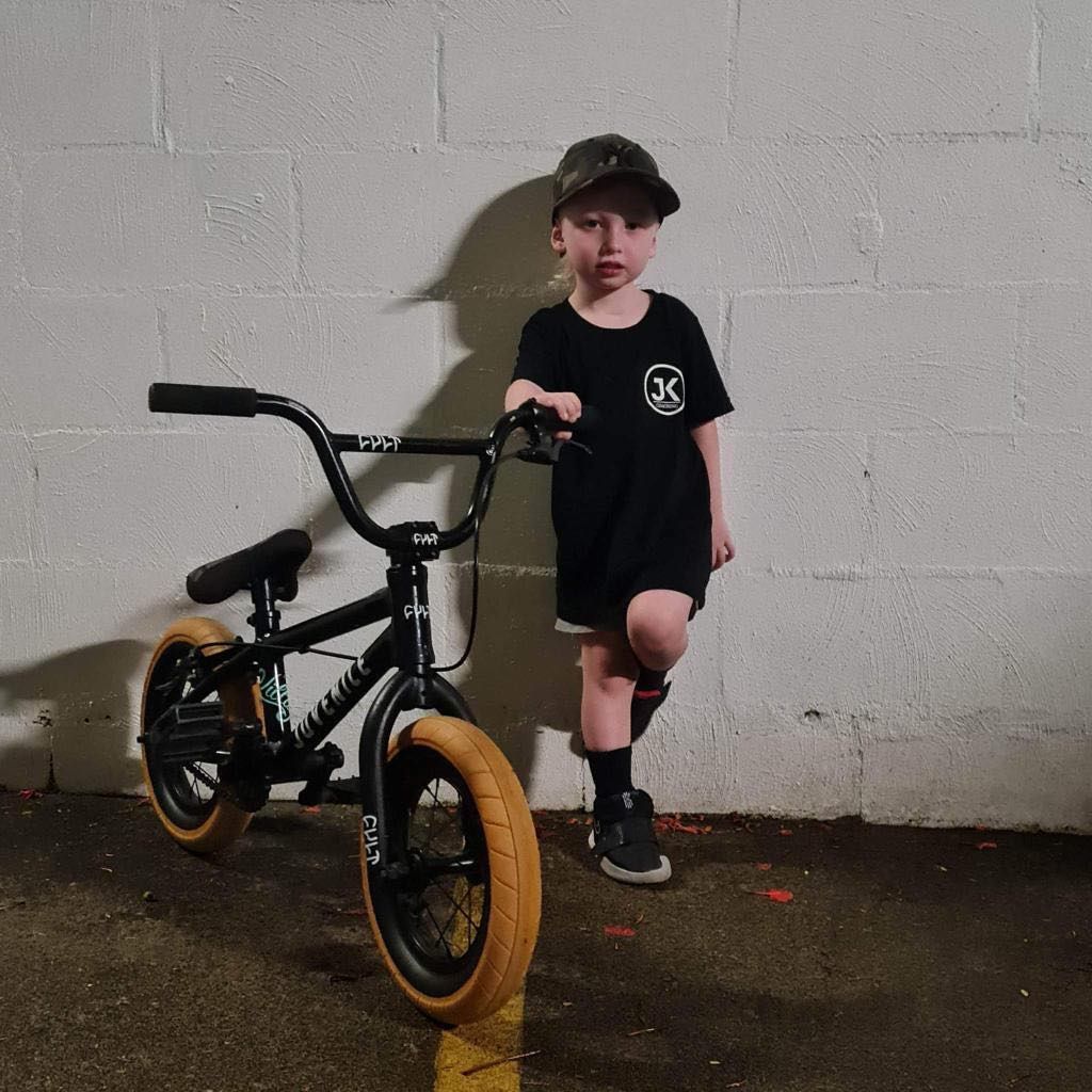 A young boy is standing next to a bmx bike.