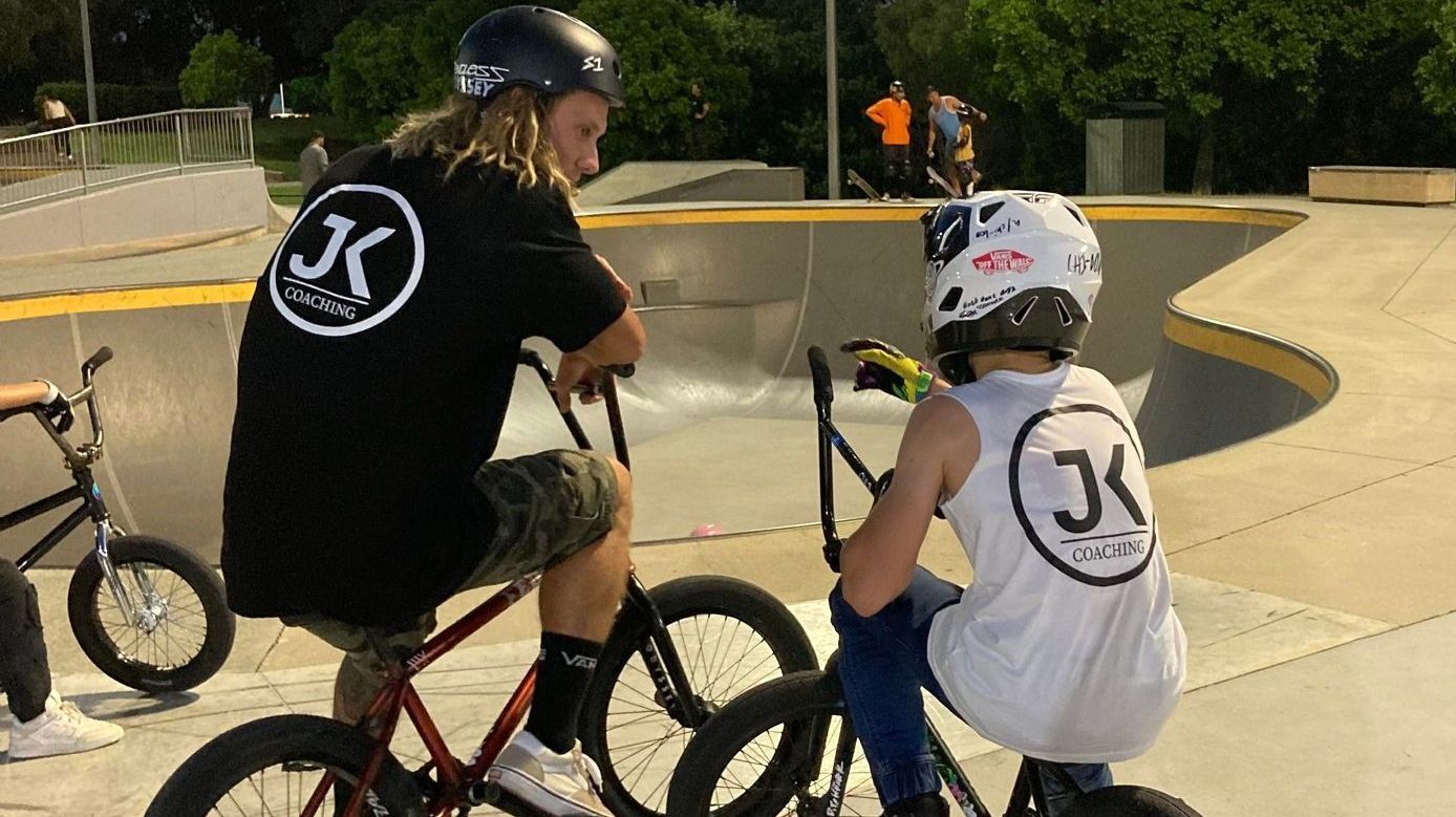 A man and a boy are riding bicycles in a skate park.
