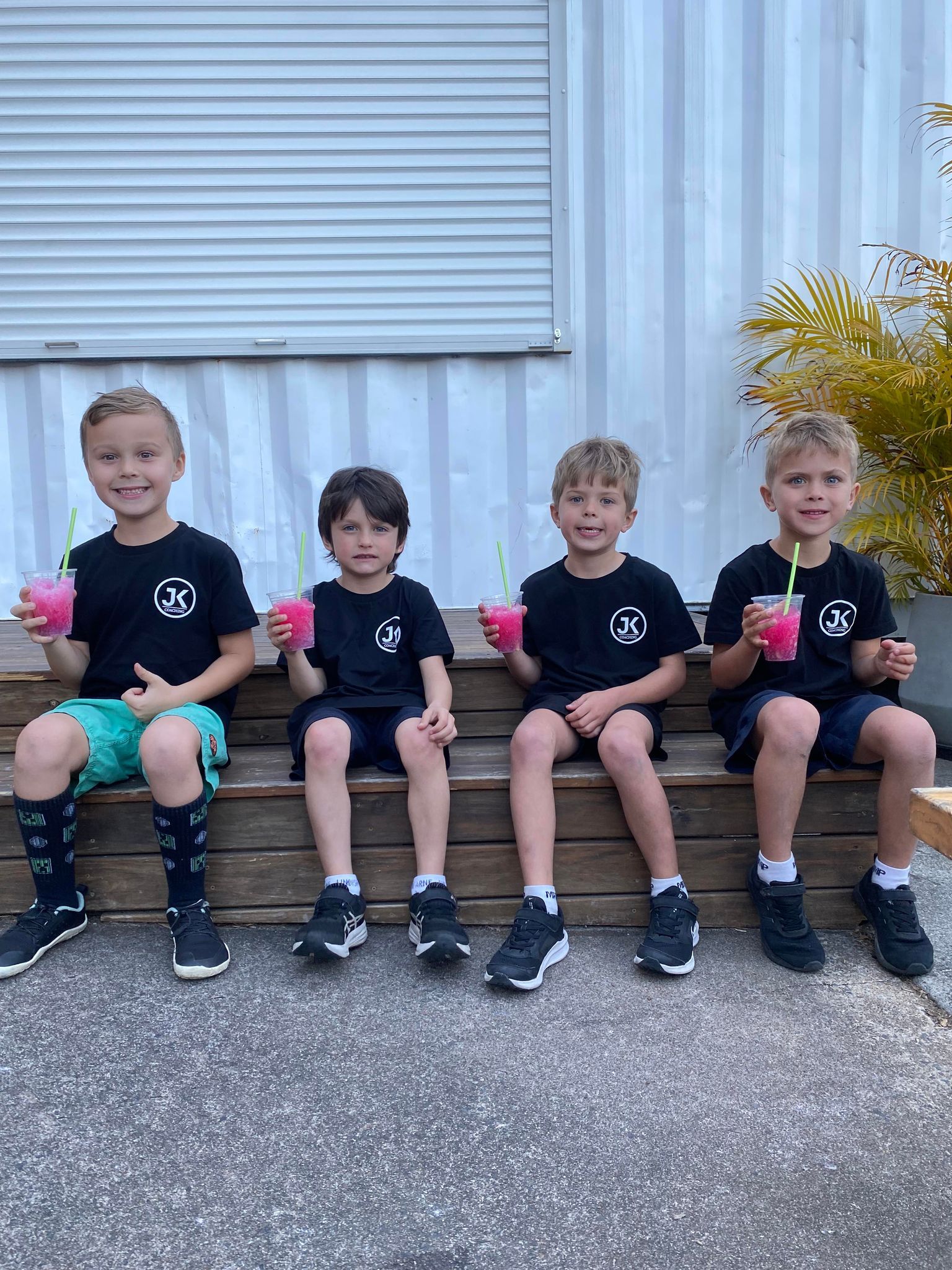 Four young boys are sitting on a wooden bench drinking slushies.