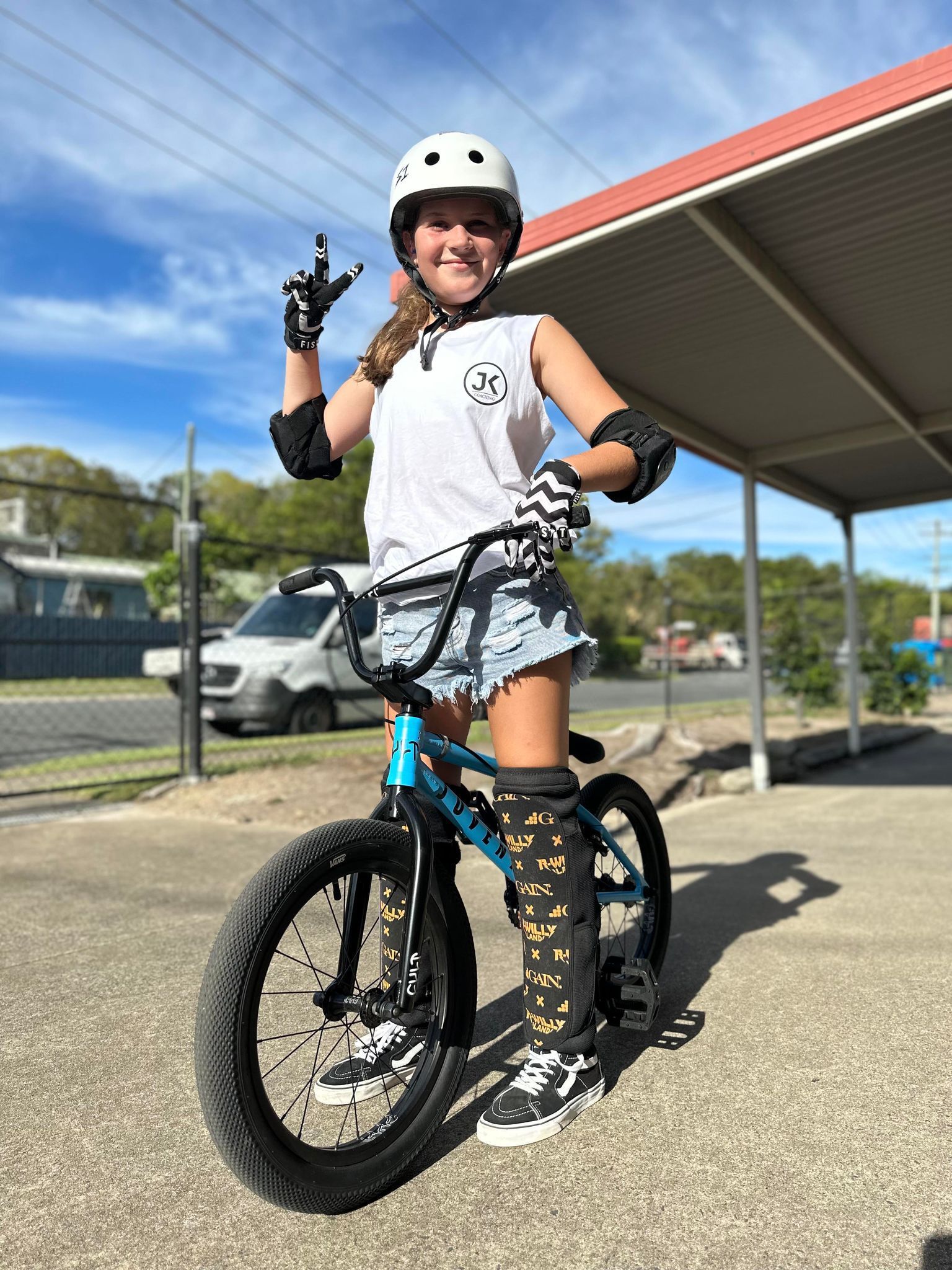A young girl is standing next to a bicycle wearing a helmet and knee pads.